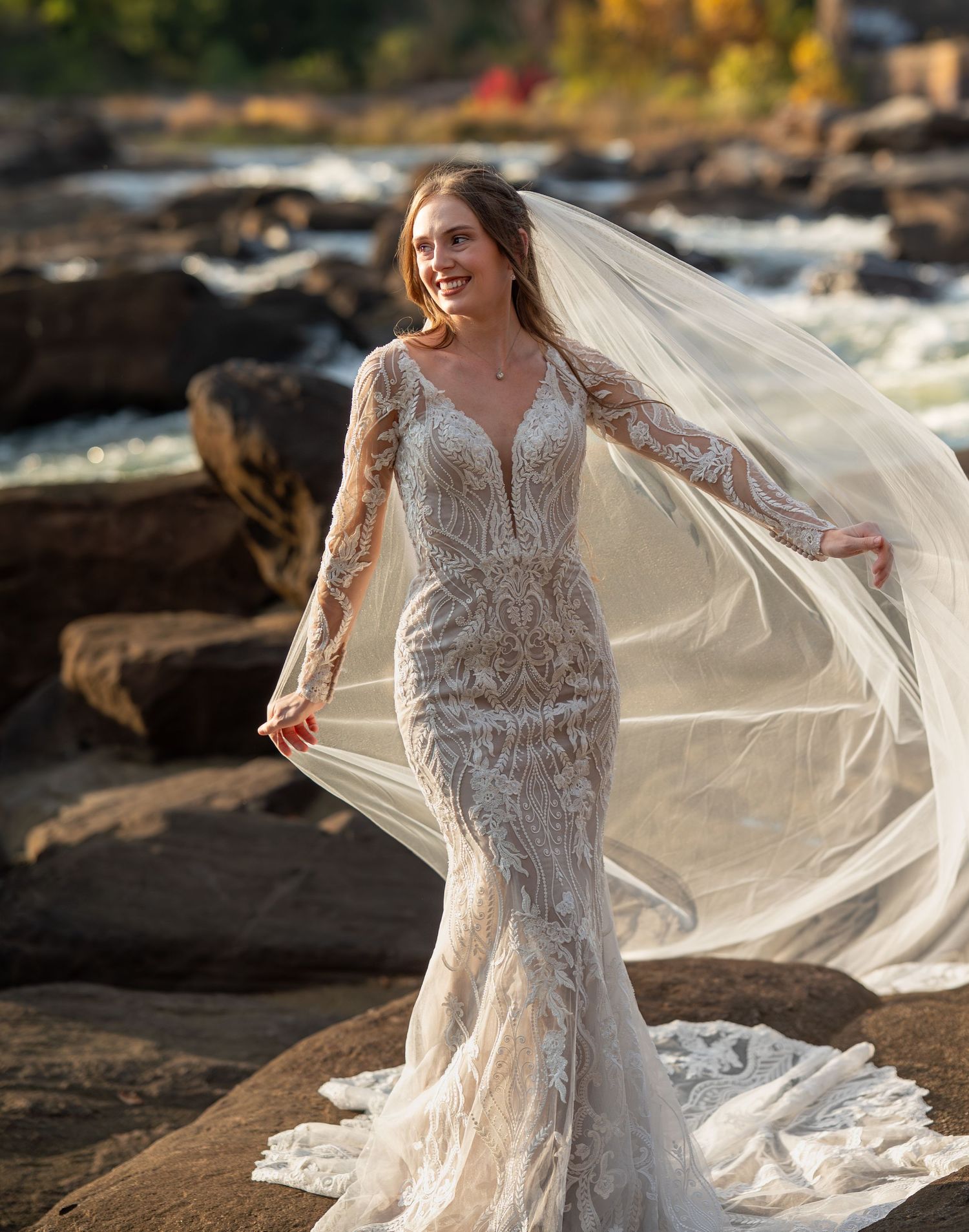 Intricate beaded wedding gown with sheer sleeves photographed against rushing water and rocks.