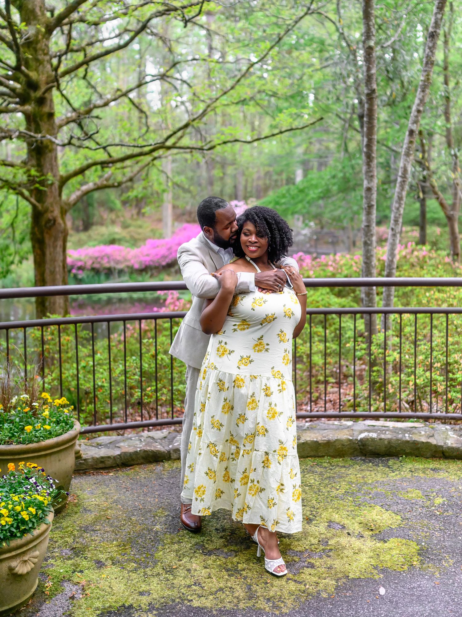 Groom hugging bride in yellow floral dress at garden wedding venue.