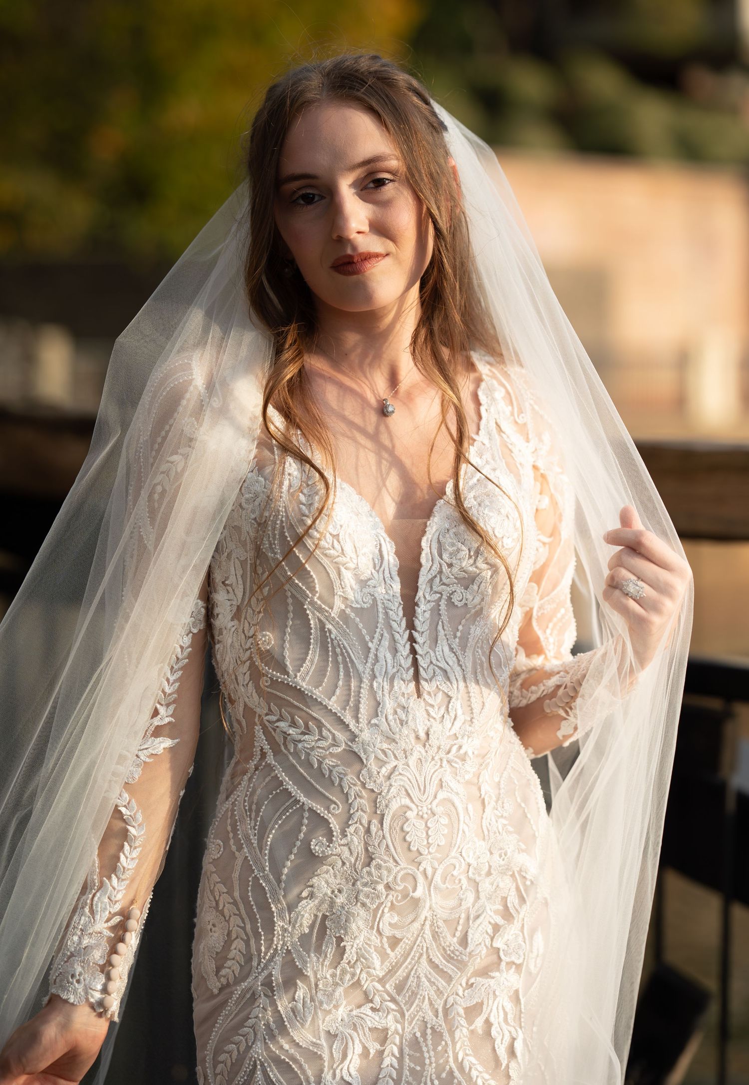 Close-up bridal portrait showcasing intricate lace details and flowing veil in warm sunlight.