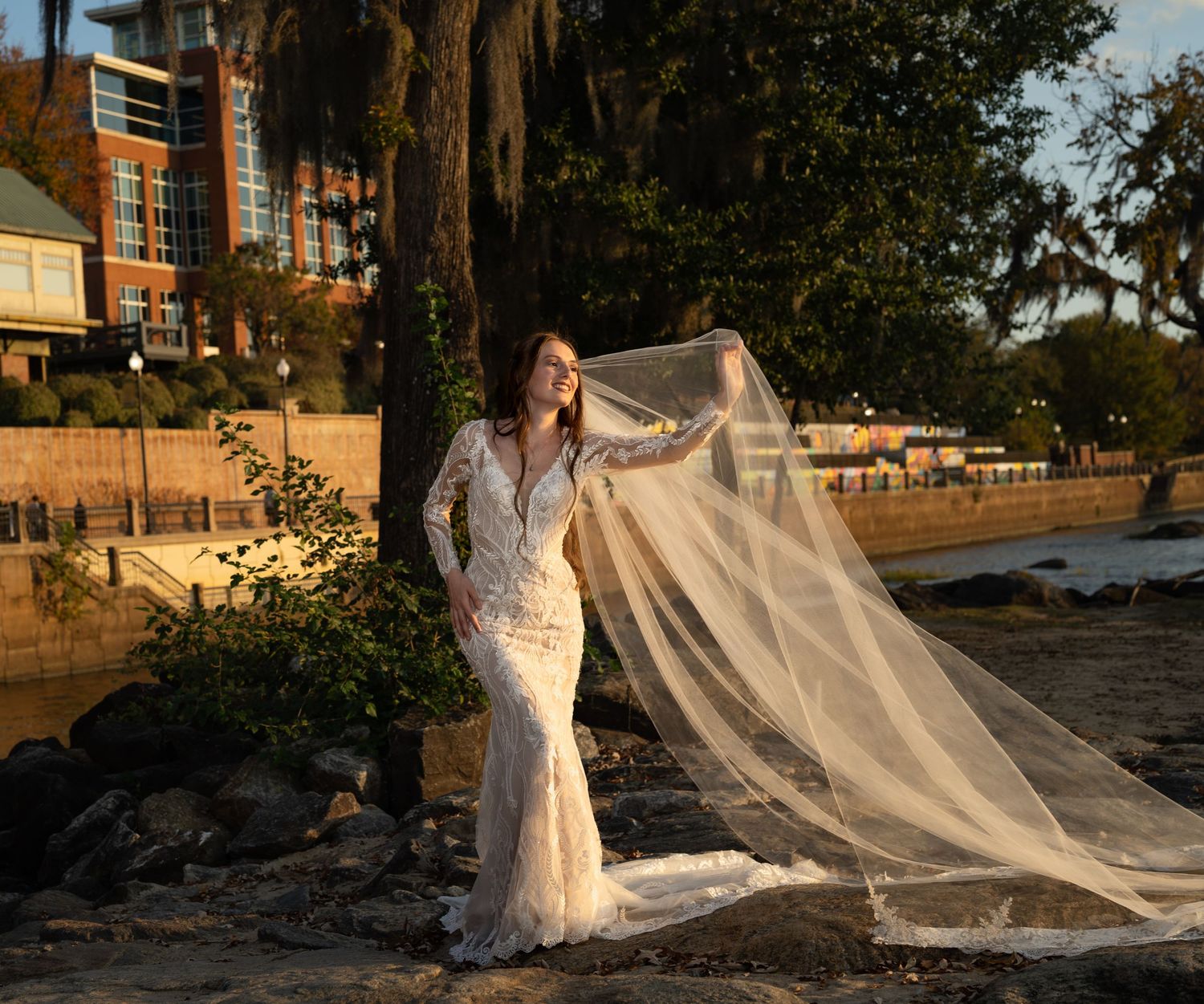 Outdoor bridal session with cathedral veil billowing near brick buildings.