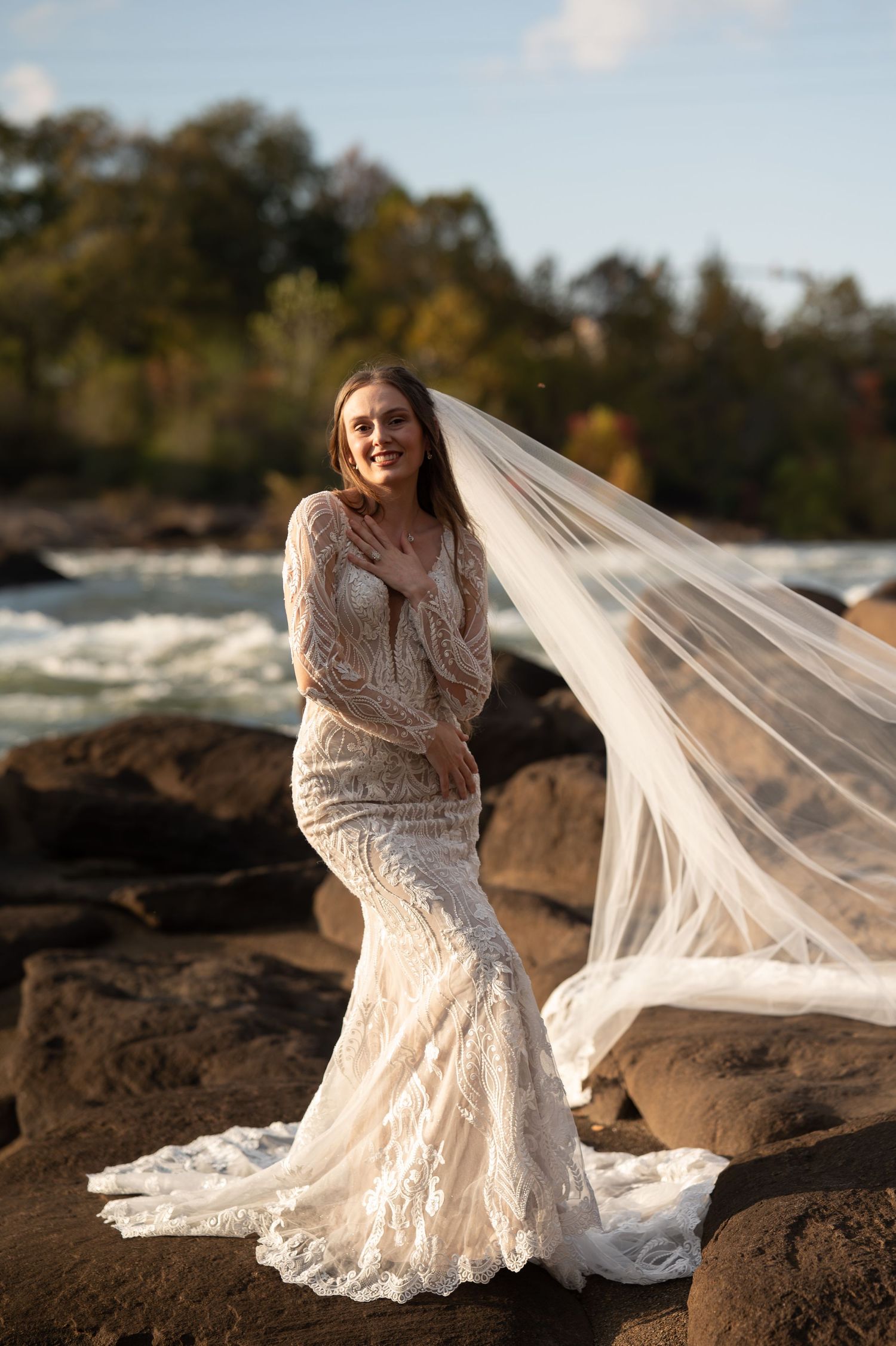 A flowing white lace wedding dress with long sleeves photographed against rocky terrain and autumn foliage.