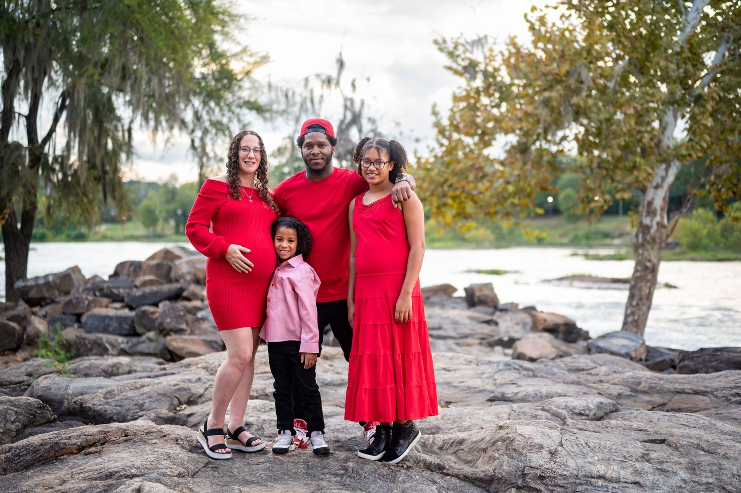 Candid family photos taken at scenic riverside location with group wearing matching red attire.