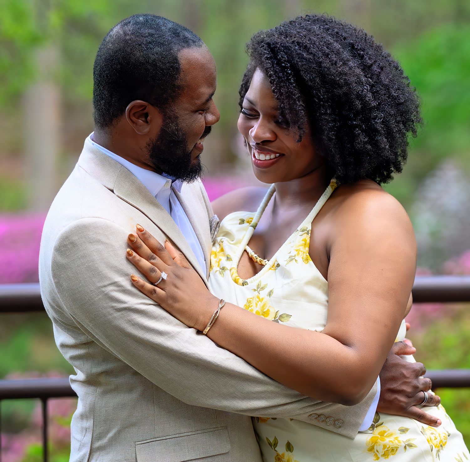 Happy engaged couple embraces and smiles at each other in a lush spring garden setting.