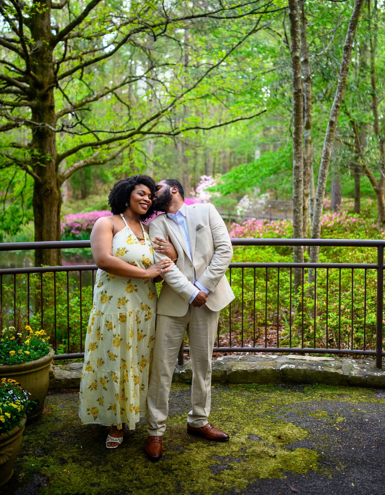 A couple shares a romantic moment on a moss-covered terrace surrounded by blooming spring trees and colorful azaleas.