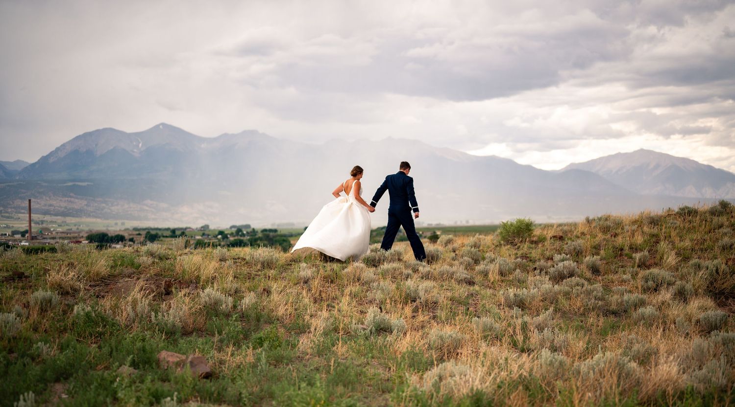 Air Force Husband and wife running together in a field in front of a huge Colorado mountain. The bride and groom look magical with the light