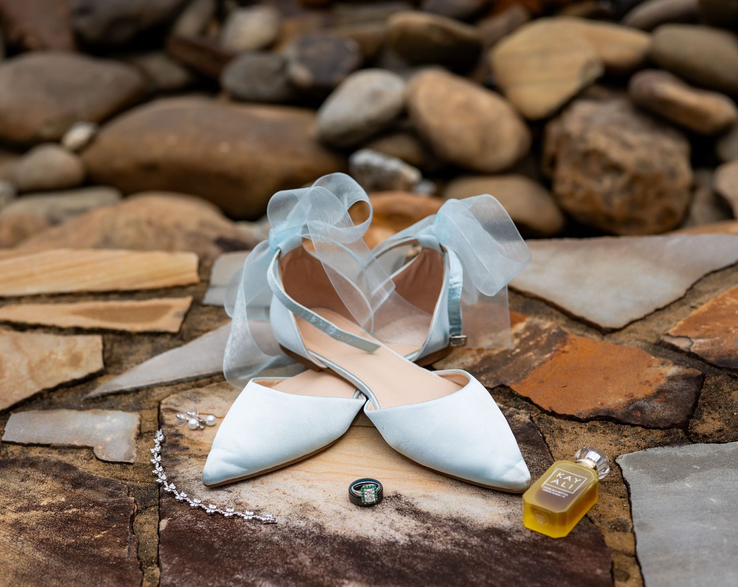 Wedding accessories including white shoes and jewelry arranged on rustic stone surface.