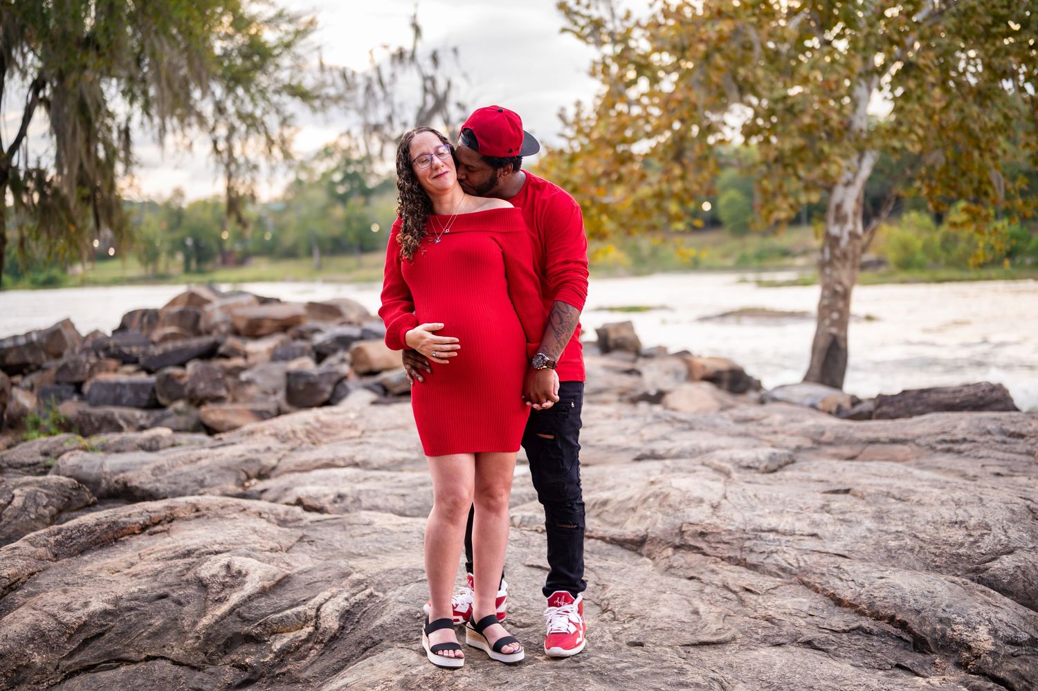 A couple in coordinated red outfits shares a joyful moment on natural rock formations outdoors.