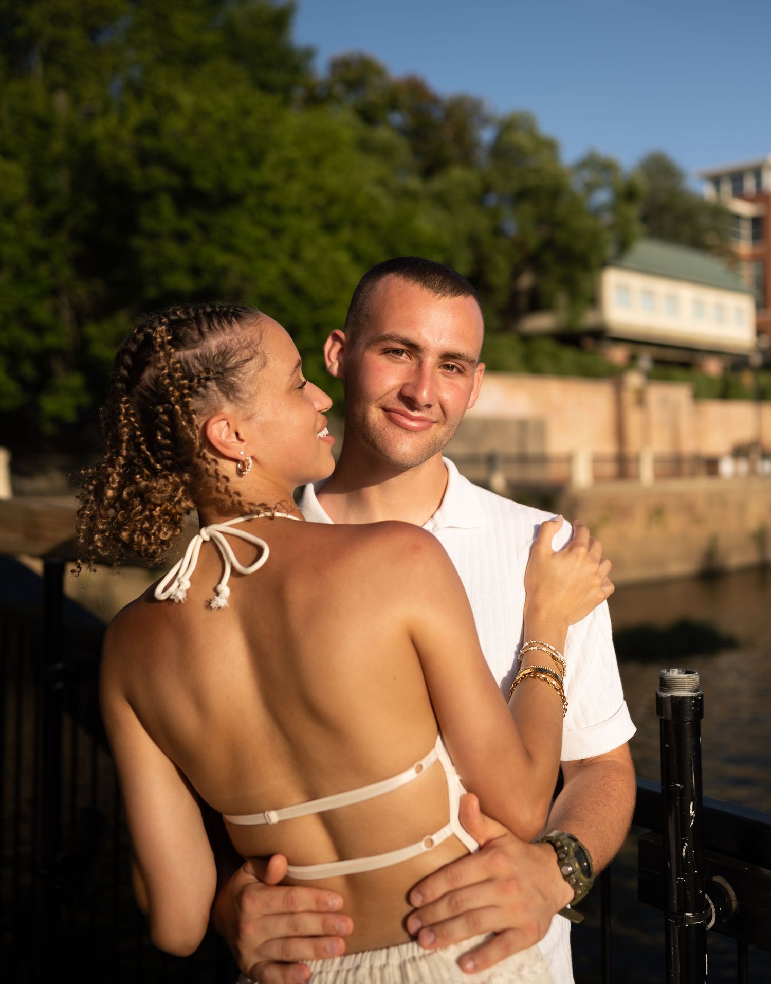 A happy couple embraces and laughs together by the water during a romantic sunset photoshoot.