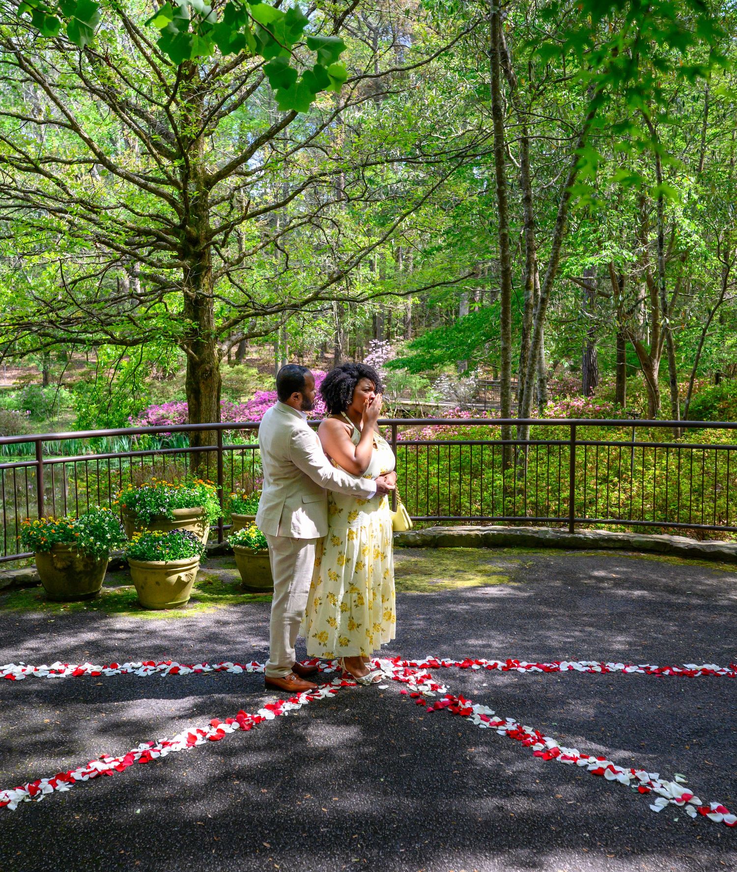 Couple embraces on a petal-decorated patio during a romantic outdoor marriage proposal in a lush garden.