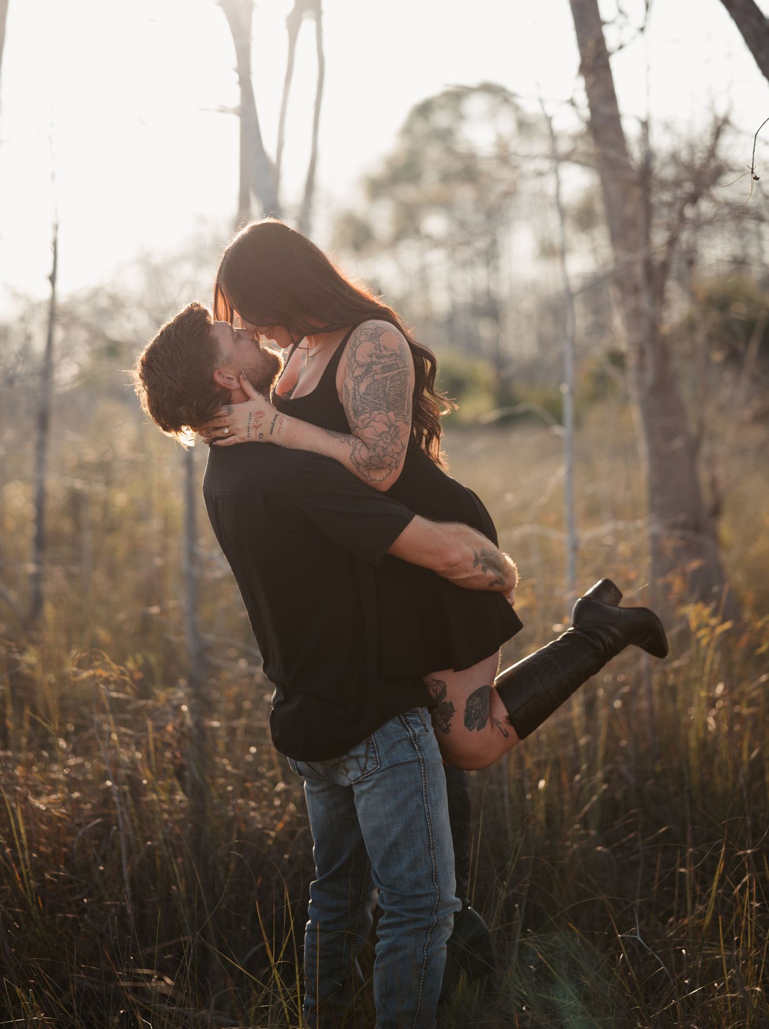 Couple sharing a romantic embrace in a field during golden hour lighting.