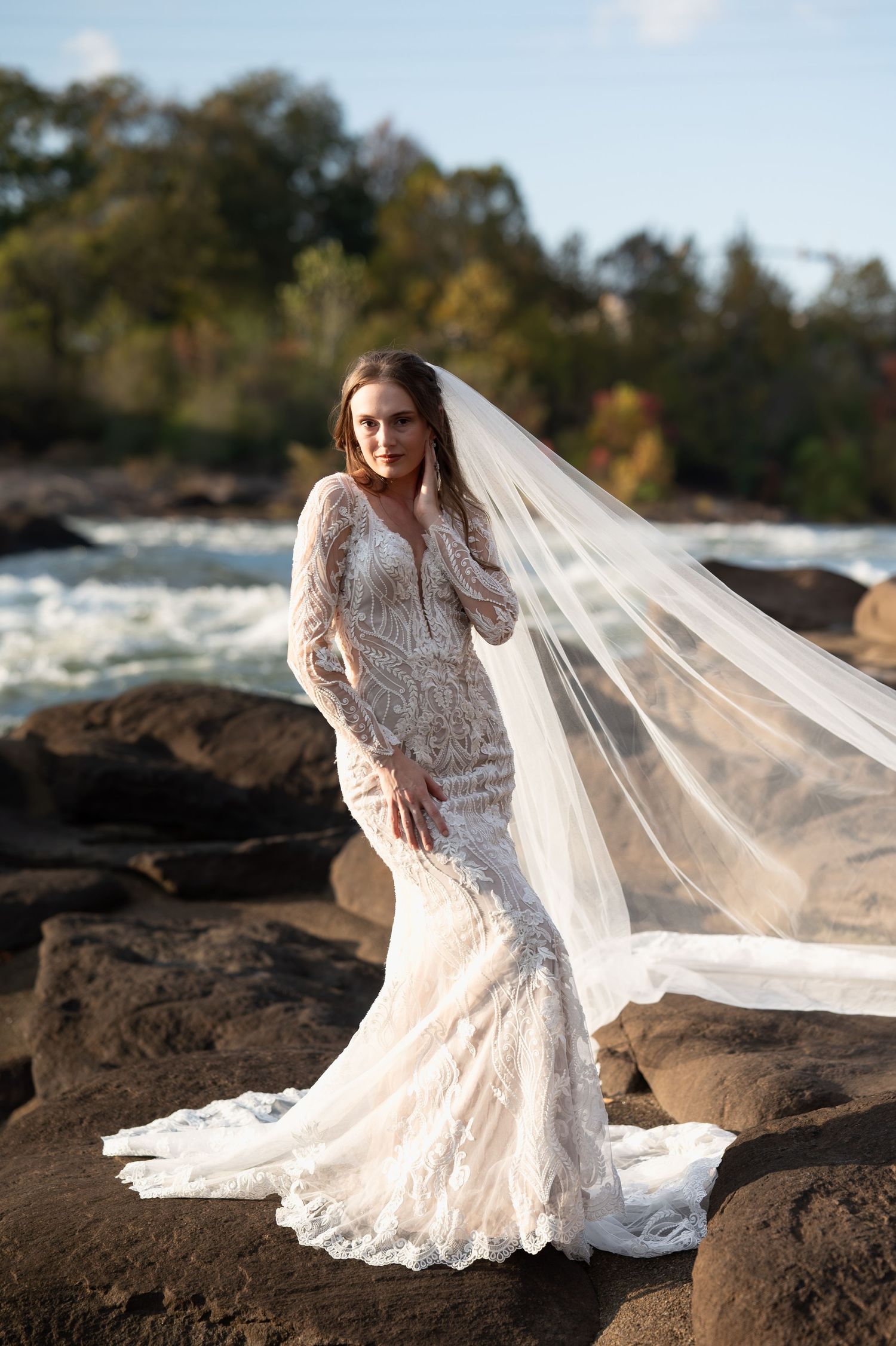 Stunning mermaid wedding dress with delicate lace details and flowing veil on rocky terrain.