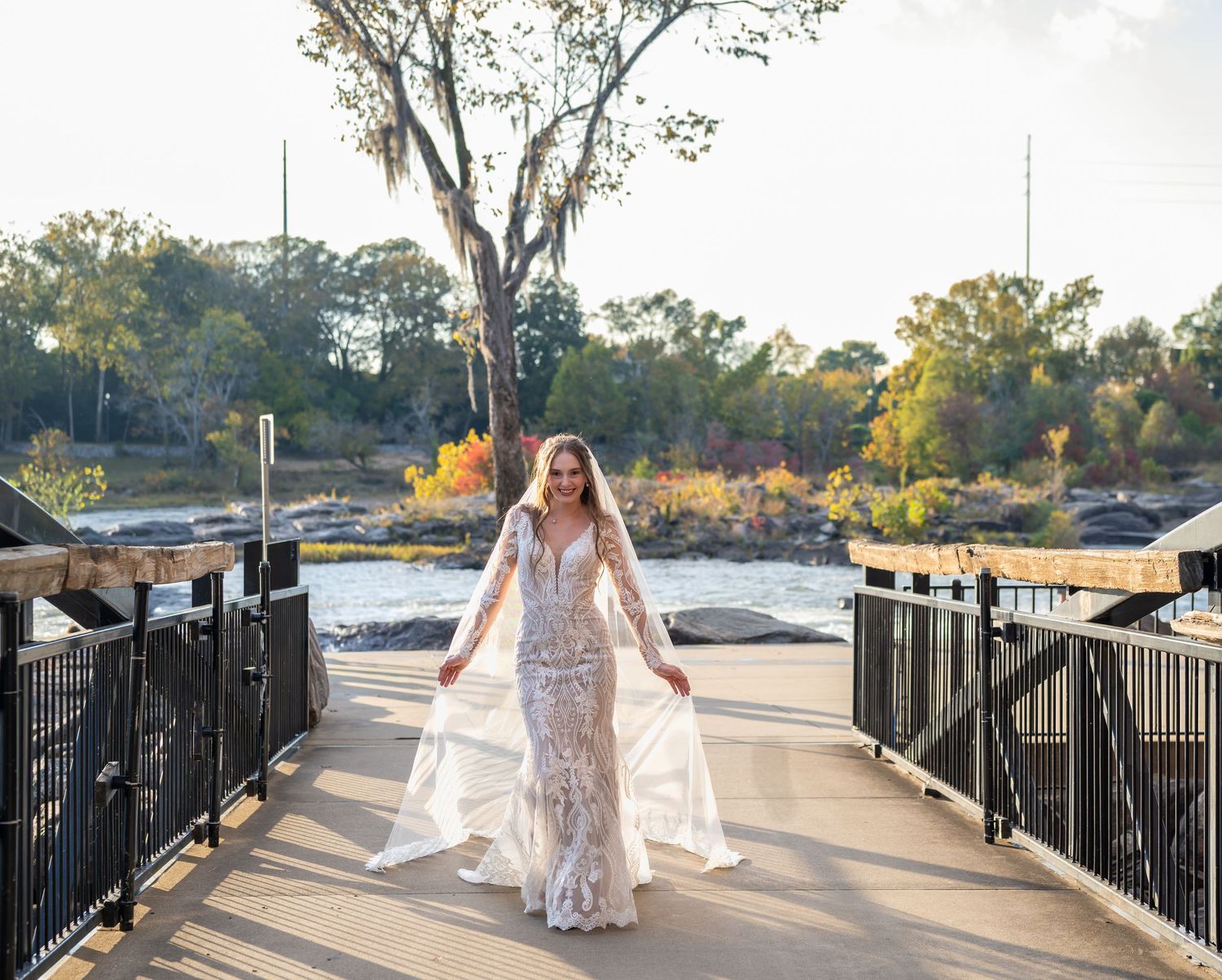 Wedding dress photoshoot along riverside walkway with iron railings at golden hour.