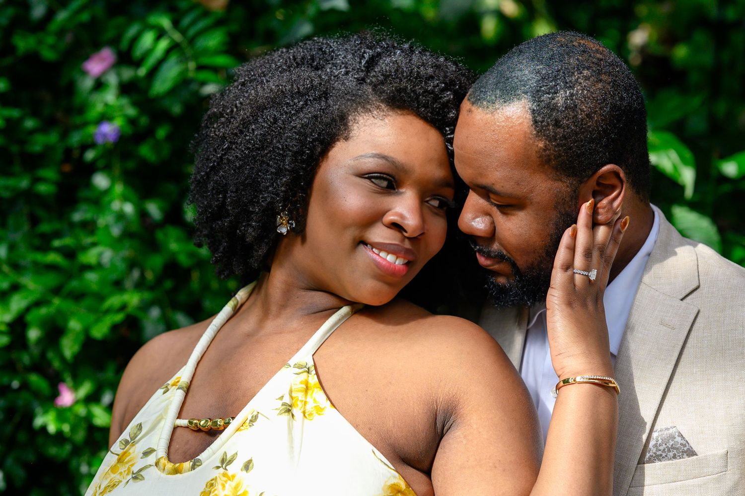 Close-up of a couple sharing a tender moment surrounded by vibrant green leaves outdoors.