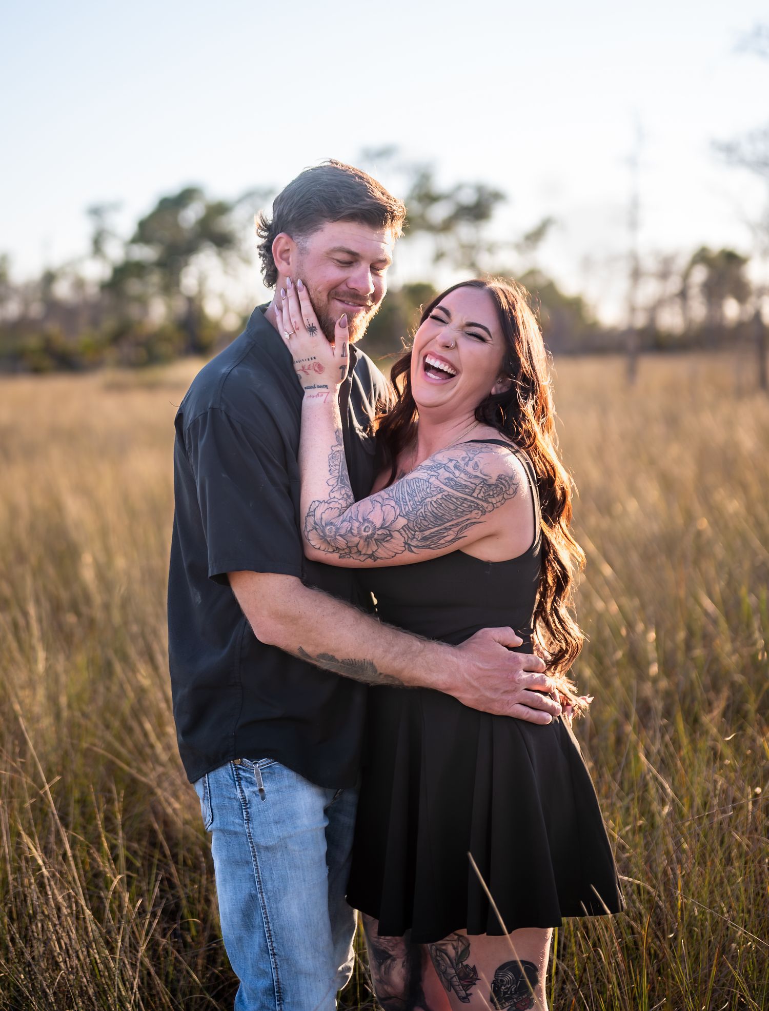 Playful couple laughing and embracing in a sunlit meadow during sunset.