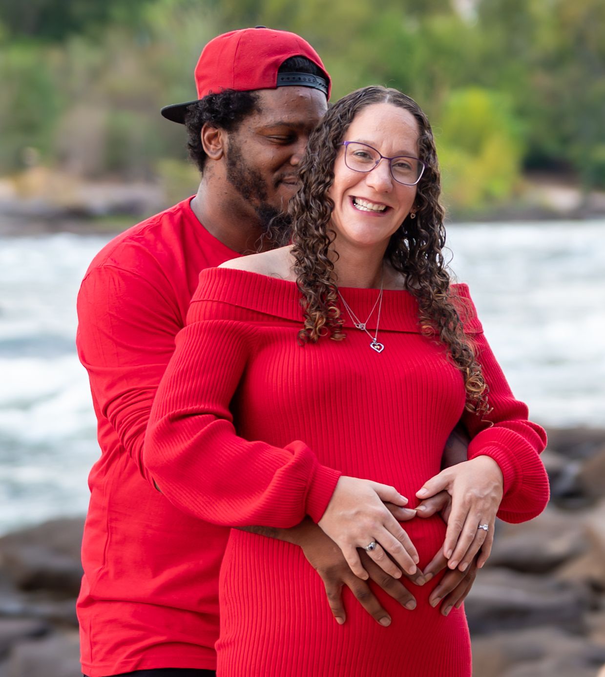 People in matching red sweaters embrace while standing near a rocky shoreline.