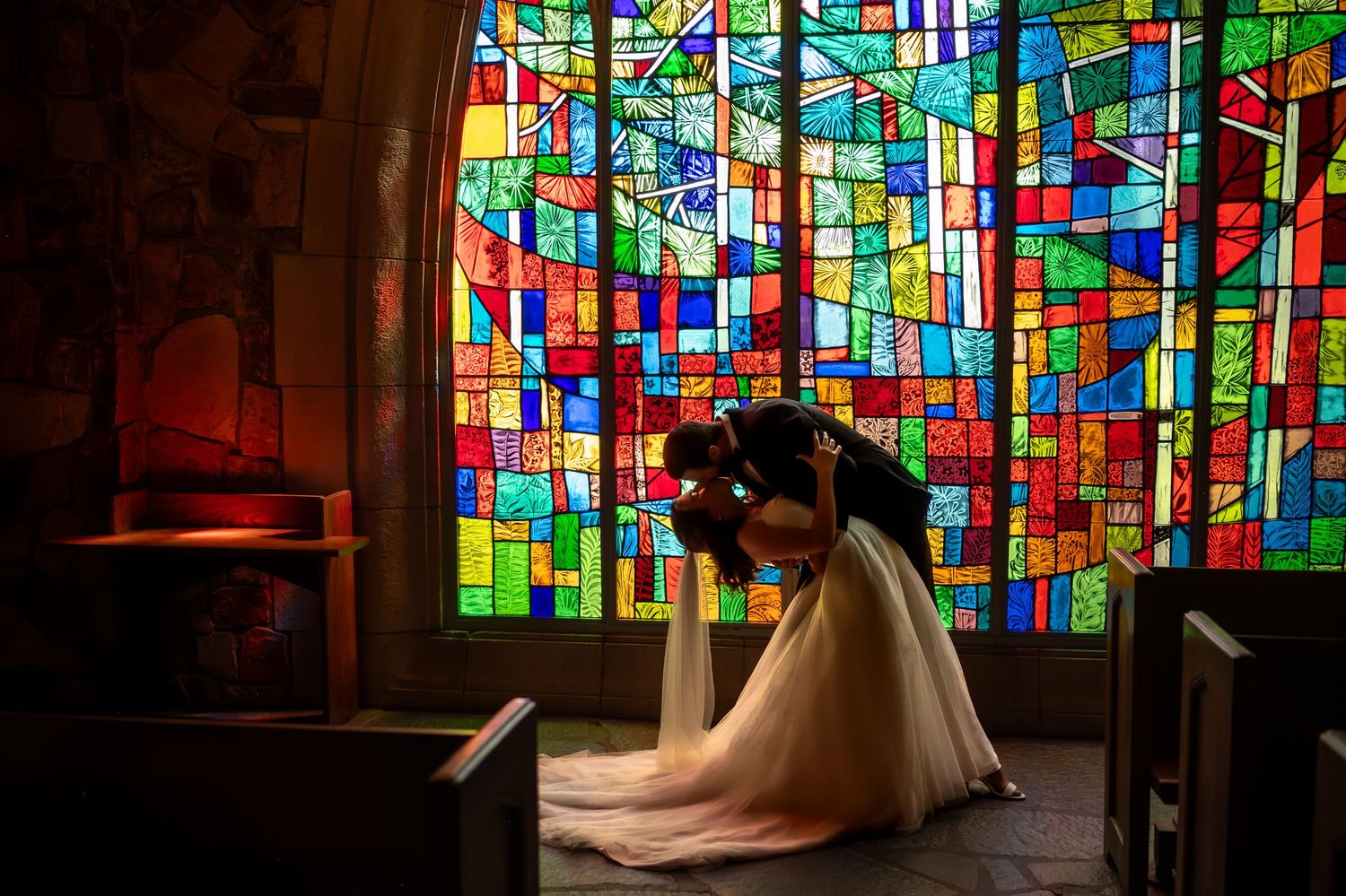 Colorful stained glass windows create a vibrant mosaic pattern in a dimly lit interior space.