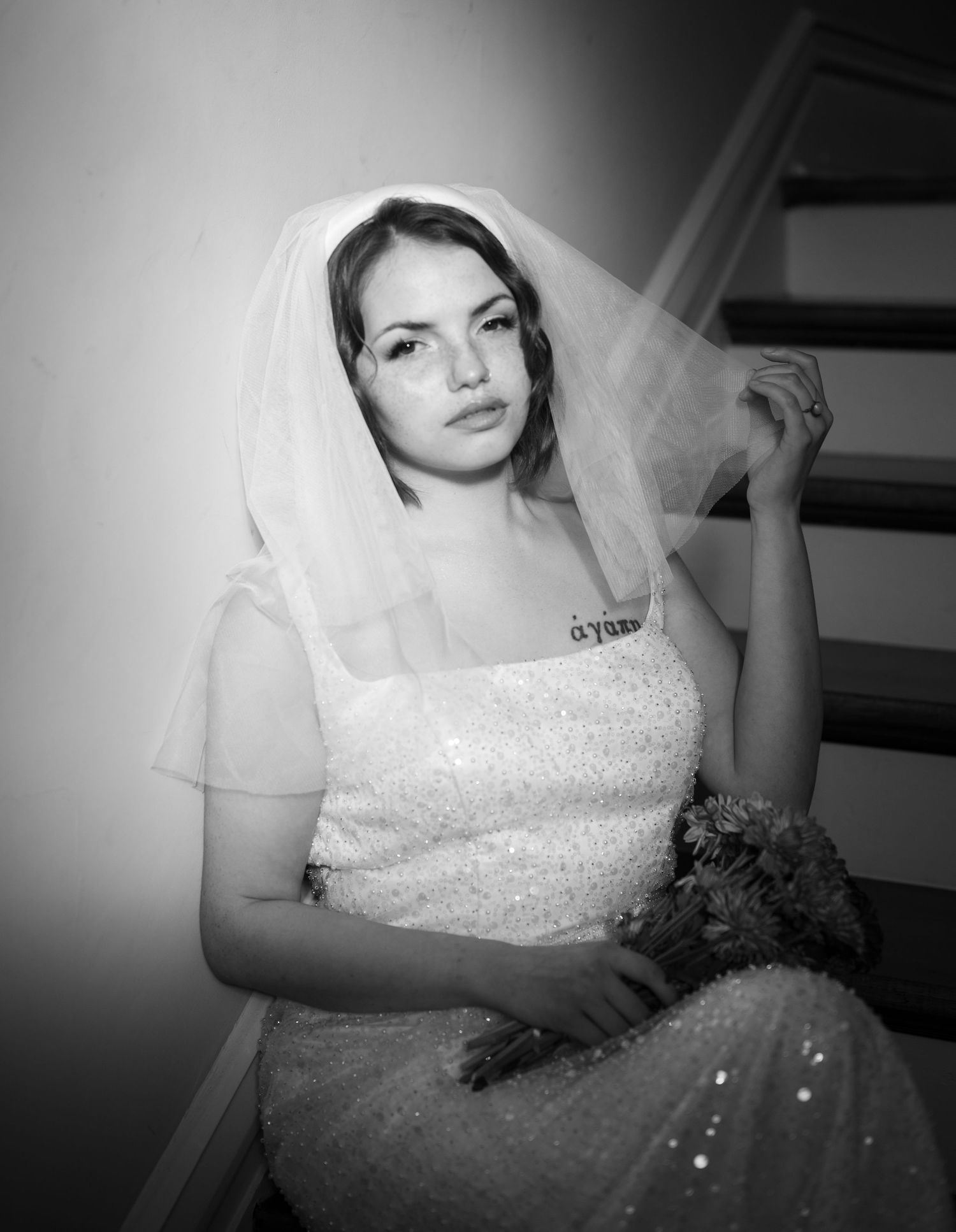 A bride in a sparkling white wedding dress and veil poses on stairs in a dramatic black and white photograph.