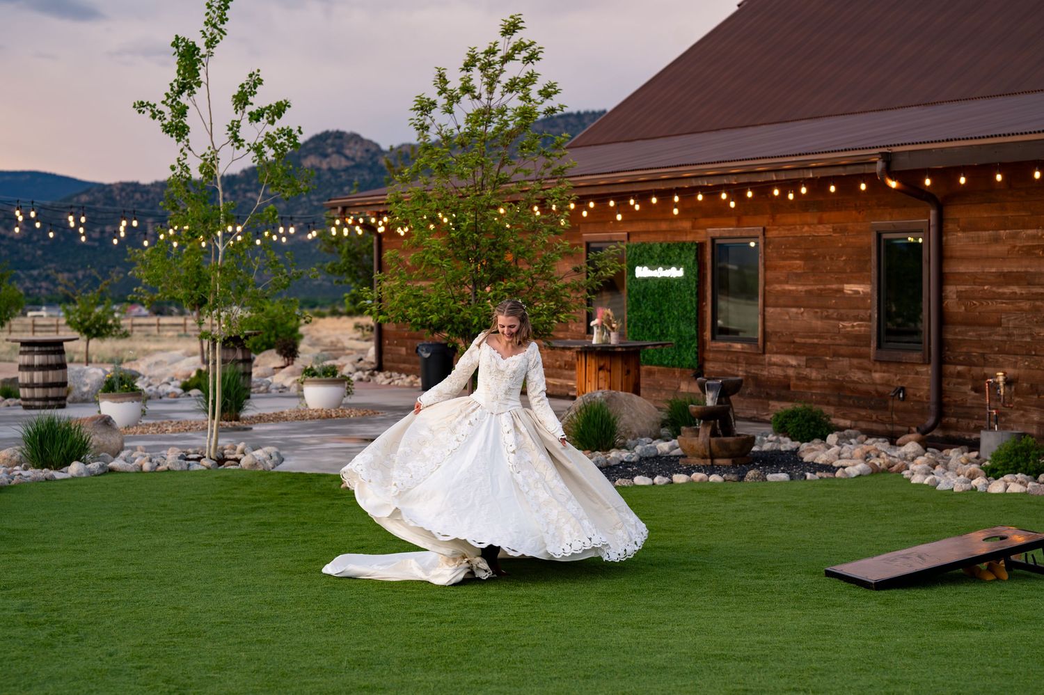 Wedding venue exterior with rustic wooden buildings and string lights at dusk.