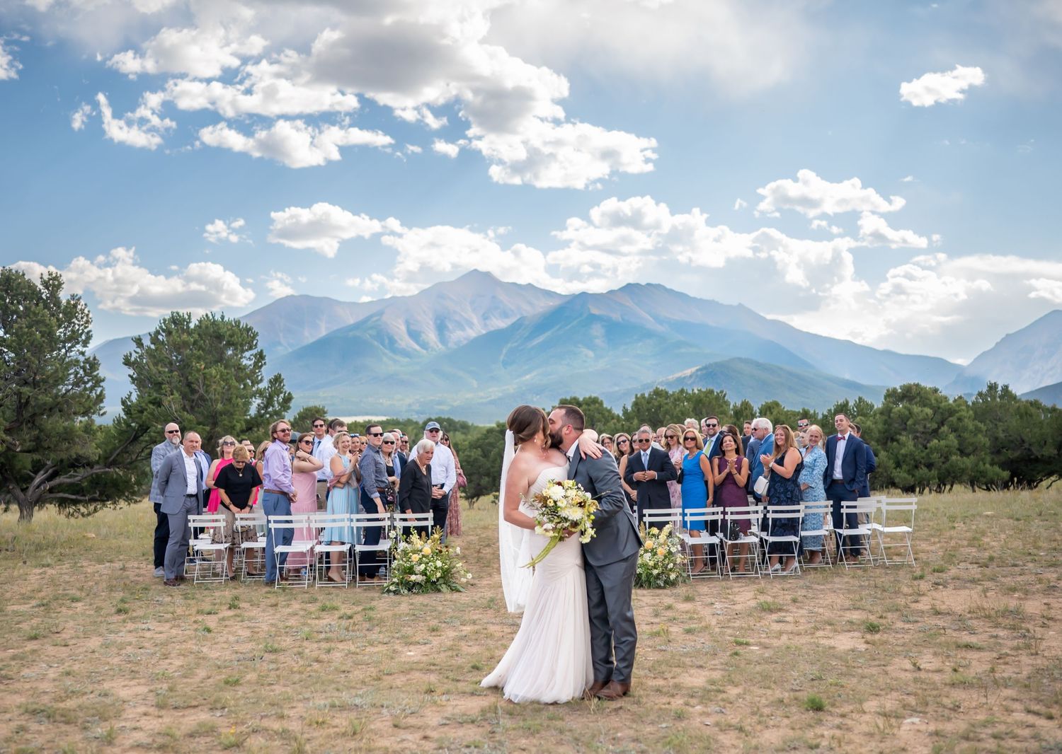 Outdoor wedding ceremony setup with mountain views and scattered clouds in the background.