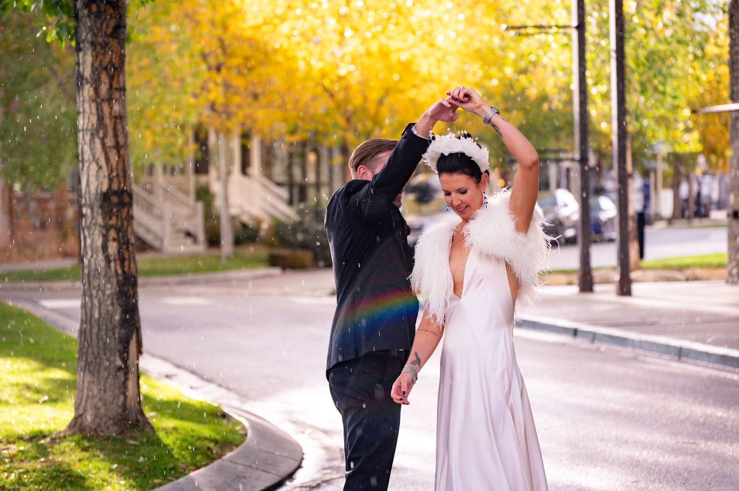 Wedding couple shares joyful moment walking along tree-lined path in autumn.