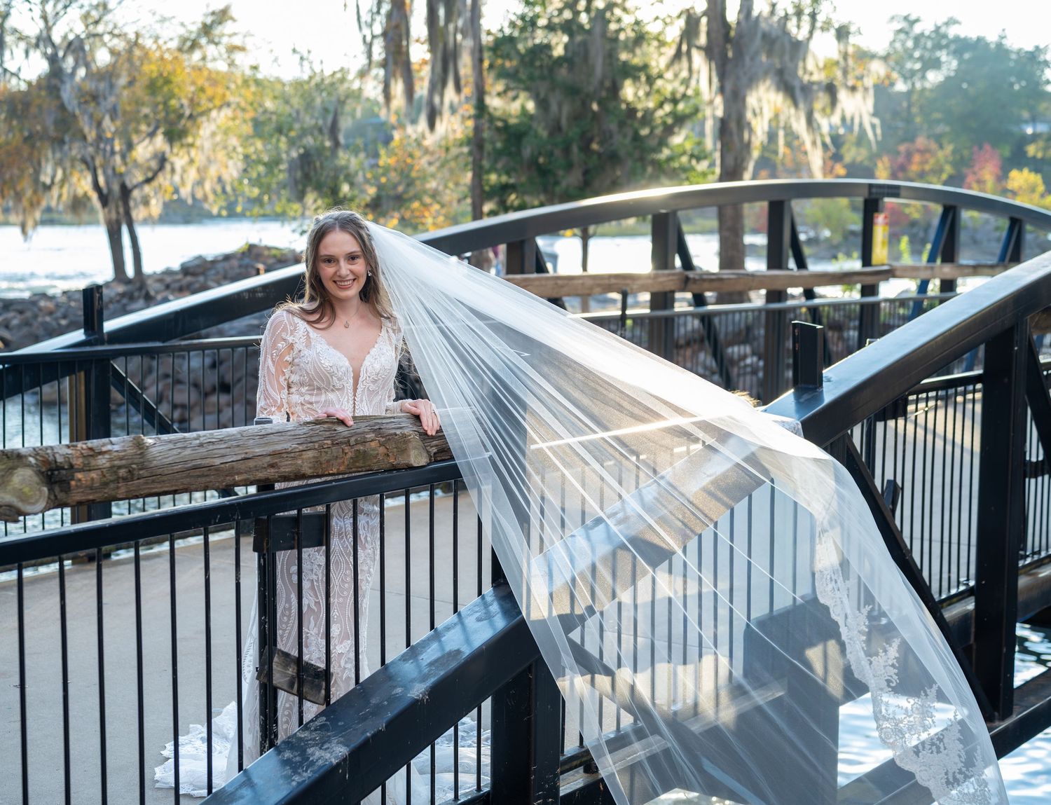 Waterfront bridal photography with dramatic veil movement along metal railings.