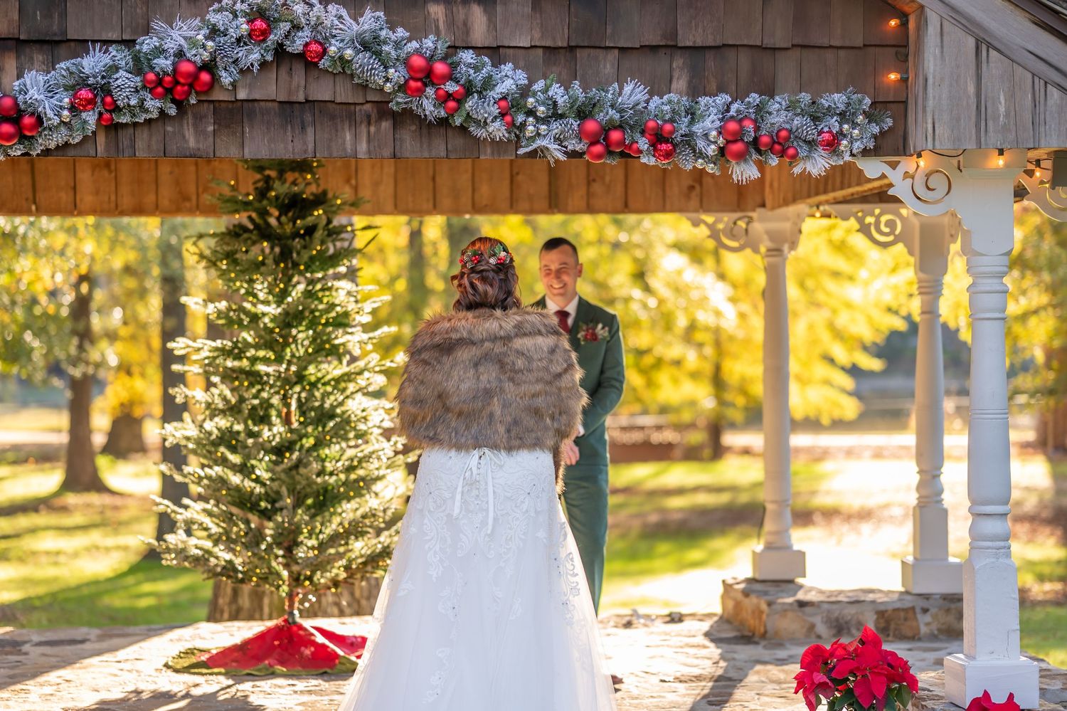 Winter wedding ceremony setup with floral arch and Christmas tree at rustic wooden venue.