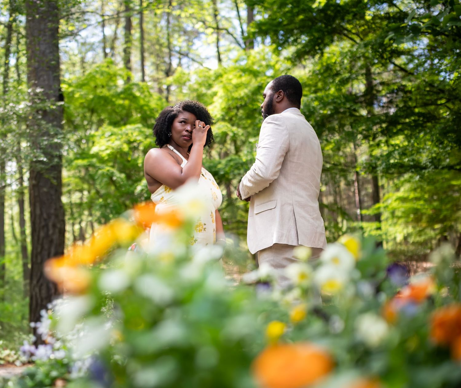 Emotional couple sharing a tender moment surrounded by colorful wildflowers in a sunlit forest.