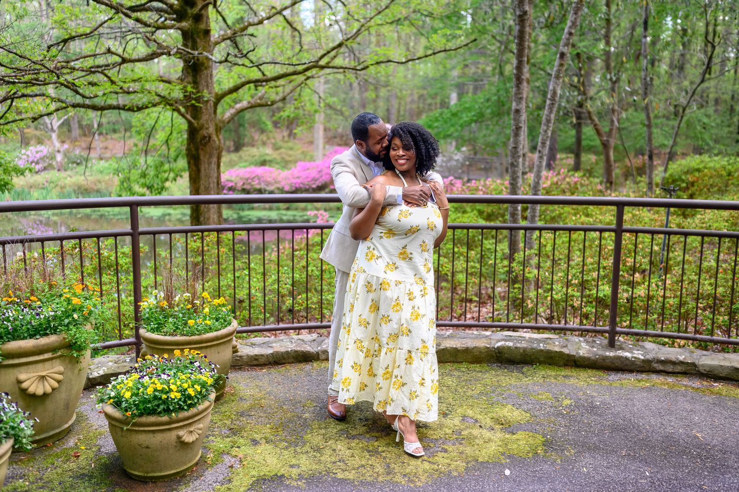 A joyful couple embraces on a garden terrace surrounded by spring flowers and lush greenery.