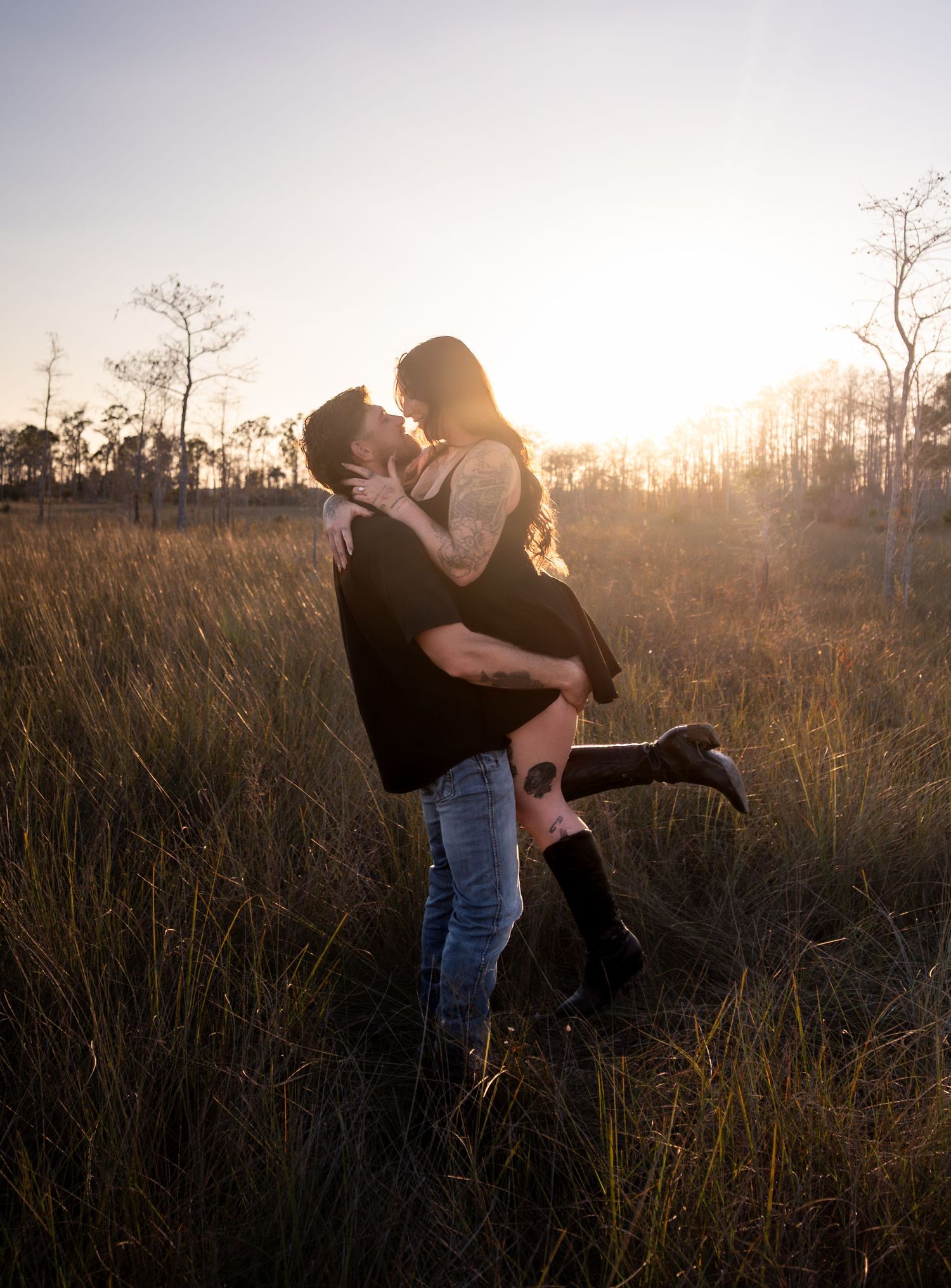 Silhouetted couple embracing in a field during sunset with trees in the background.