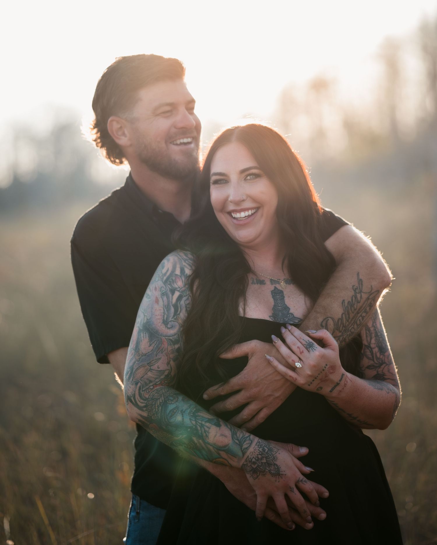 Couple sharing intimate moments in a golden sunlit field with tattoos visible on their arms.
