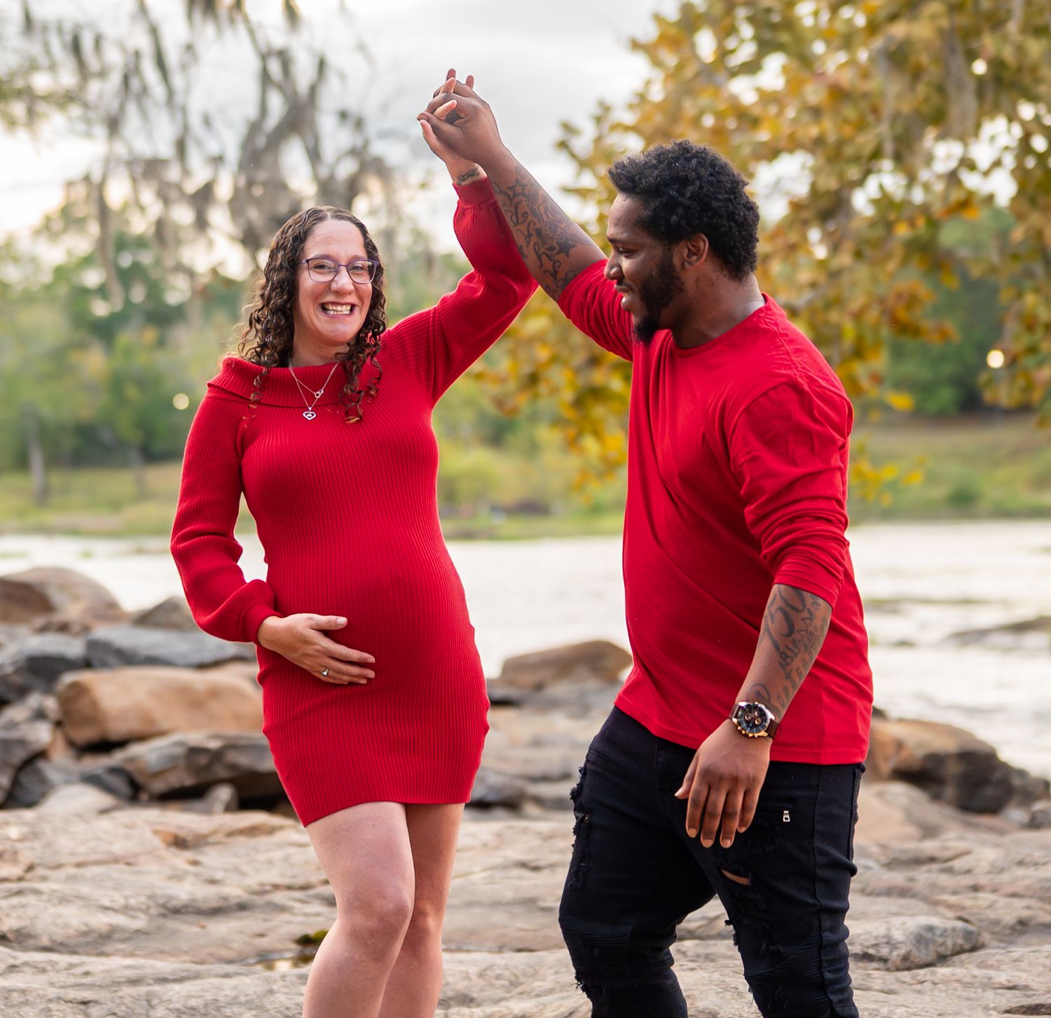 Two people in bright red clothing celebrate and laugh together on rocky terrain during a photoshoot.