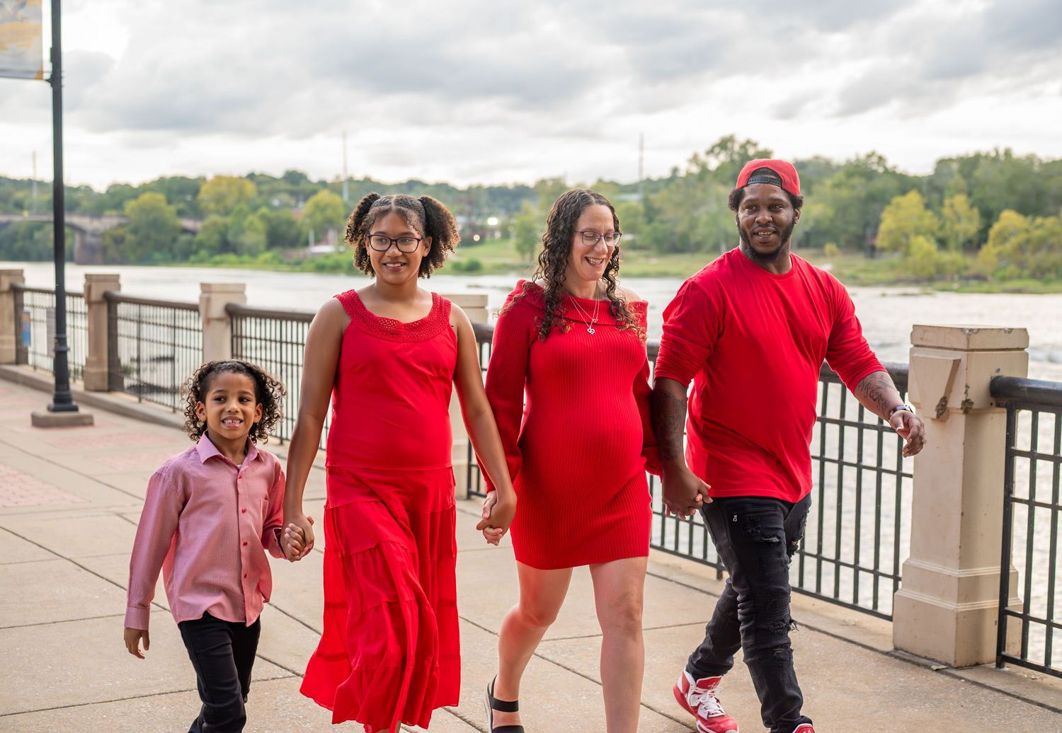 A group wearing coordinated red outfits walks together along a waterfront path on a cloudy day.