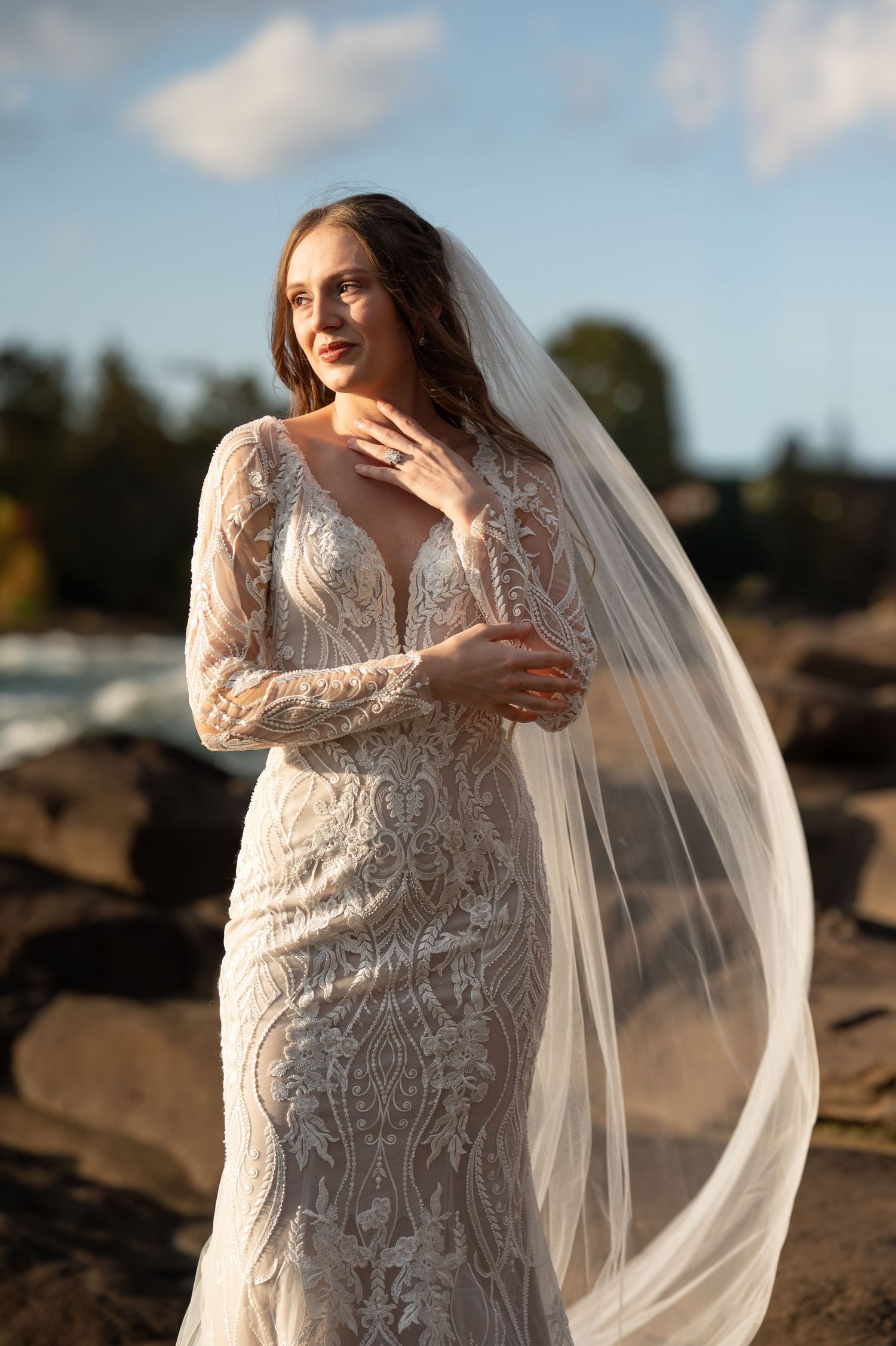 An ethereal bridal portrait showcasing a detailed lace gown with long sleeves in golden sunlight.