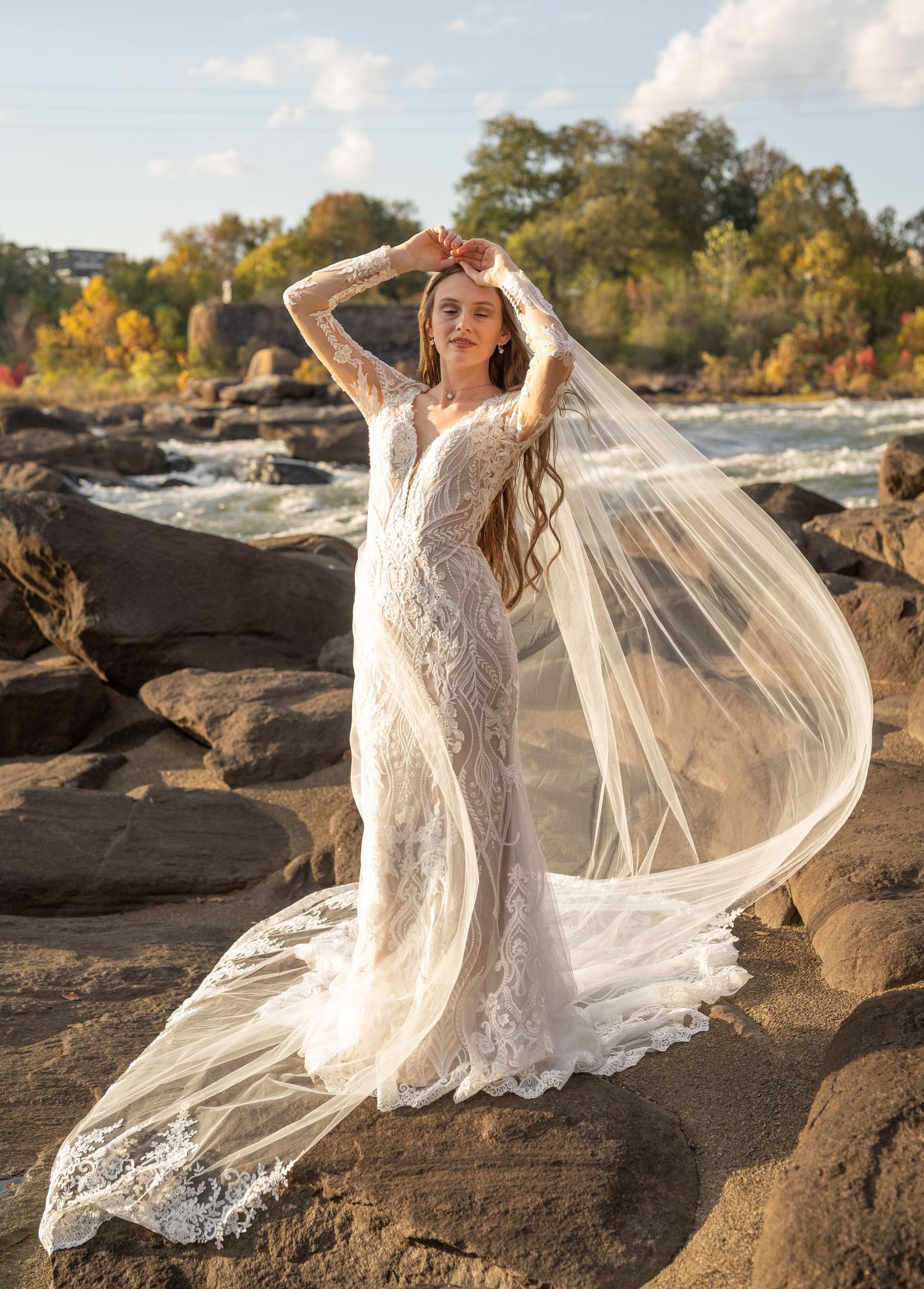 Wedding dress photoshoot on rocky landscape with billowing veil in golden light.