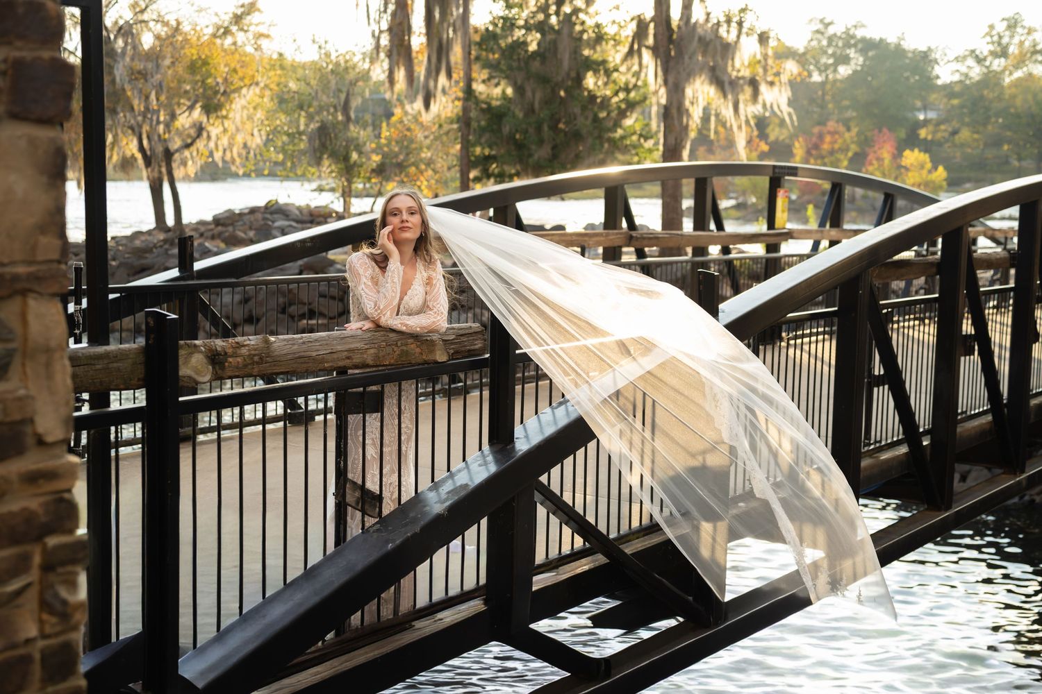 Sunset bridal portrait on wooden bridge over water with dramatic cathedral length veil.