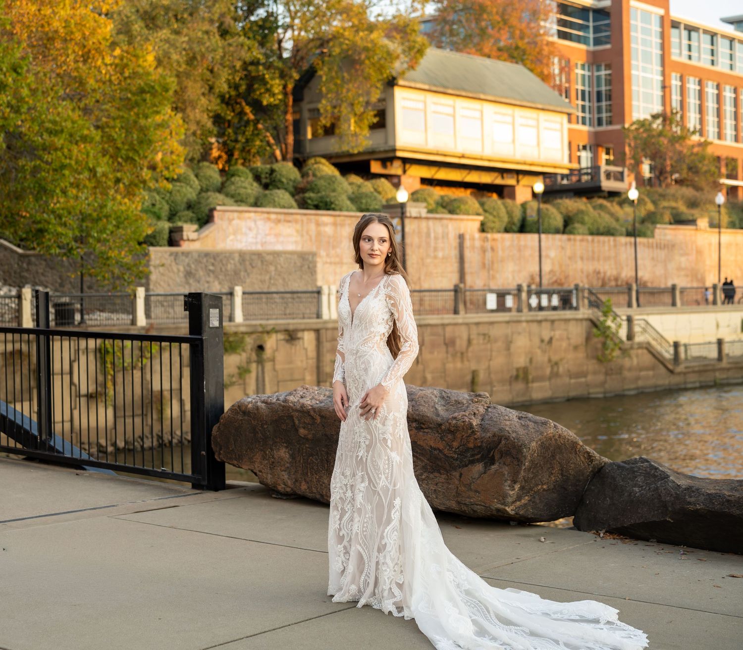Full-length view of wedding dress with train against architectural backdrop and autumn scenery.