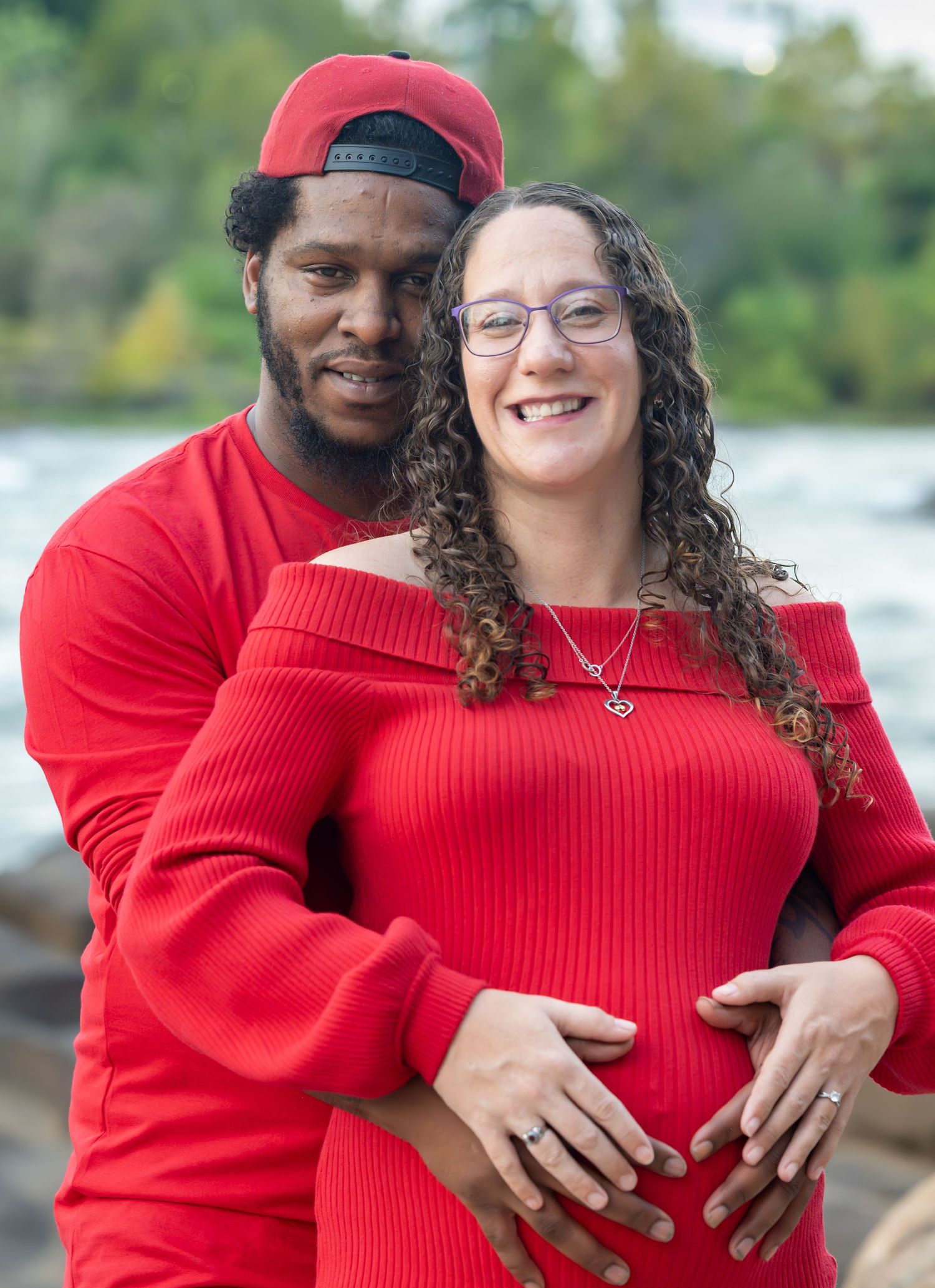 A couple wearing matching red sweaters embrace outdoors during an autumn photoshoot.