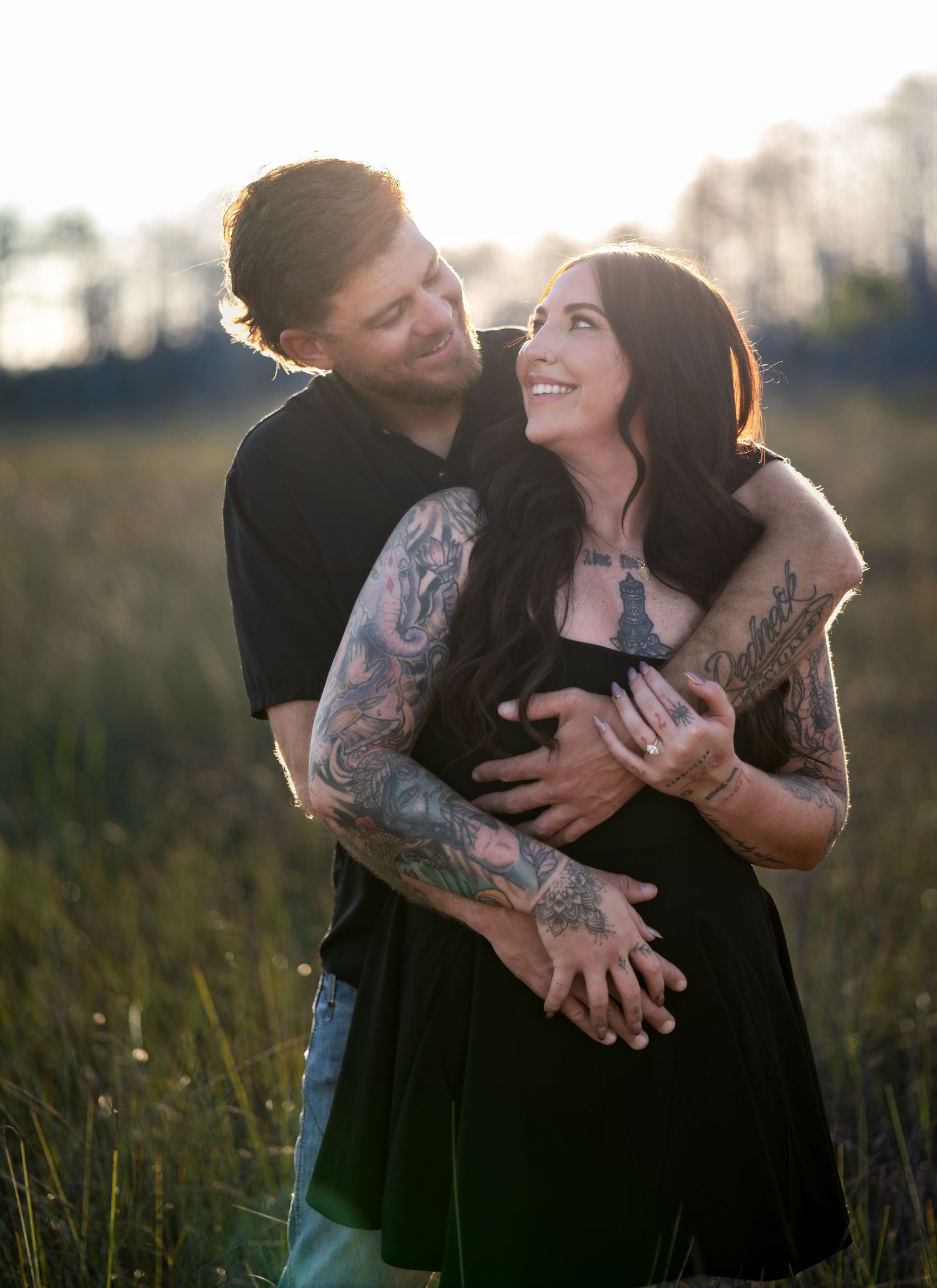 Couple embraces lovingly in field during golden hour with dramatic lighting.