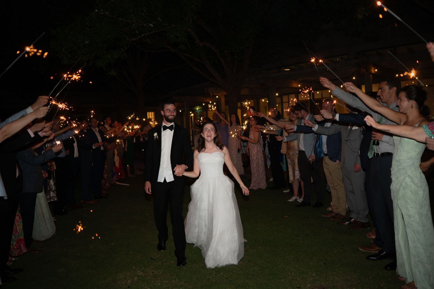 Wedding guests hold sparklers creating a magical tunnel of light for the newlyweds to walk through at nighttime.