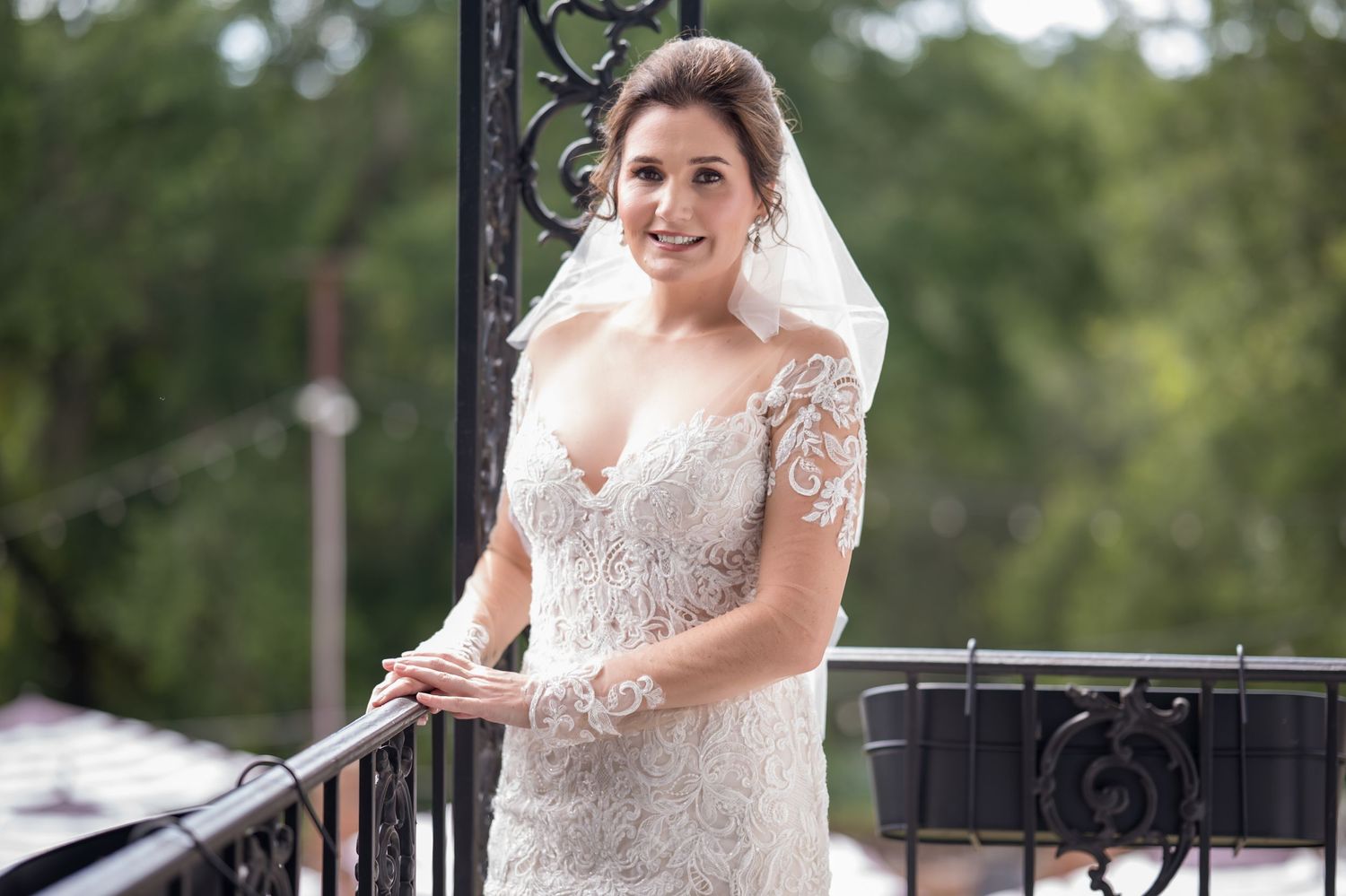 A bride in a lace wedding dress poses on an outdoor porch during a summer wedding photoshoot.