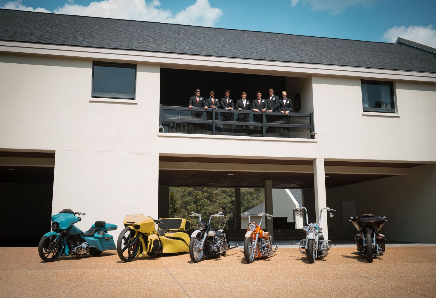 A panoramic view of a row of motorcycles parked in front of a white building under a blue sky with clouds.