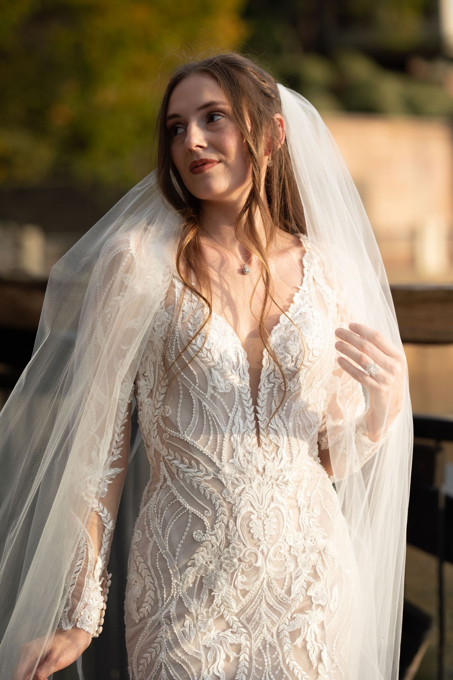 Ethereal bridal portrait featuring a delicate lace wedding gown and flowing veil in golden sunset light.