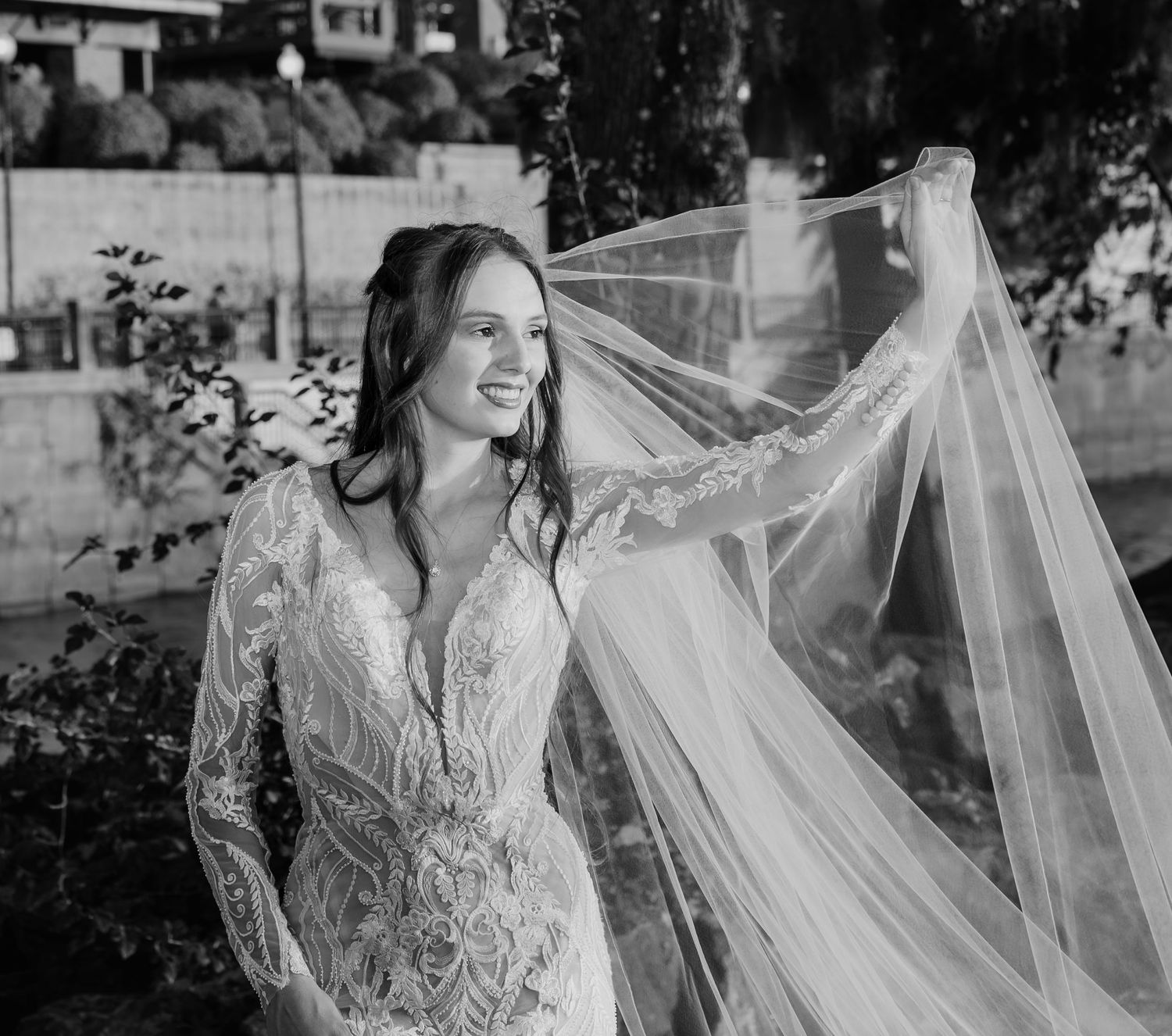 Black and white photo of a bride's veil flowing in the wind against natural scenery.