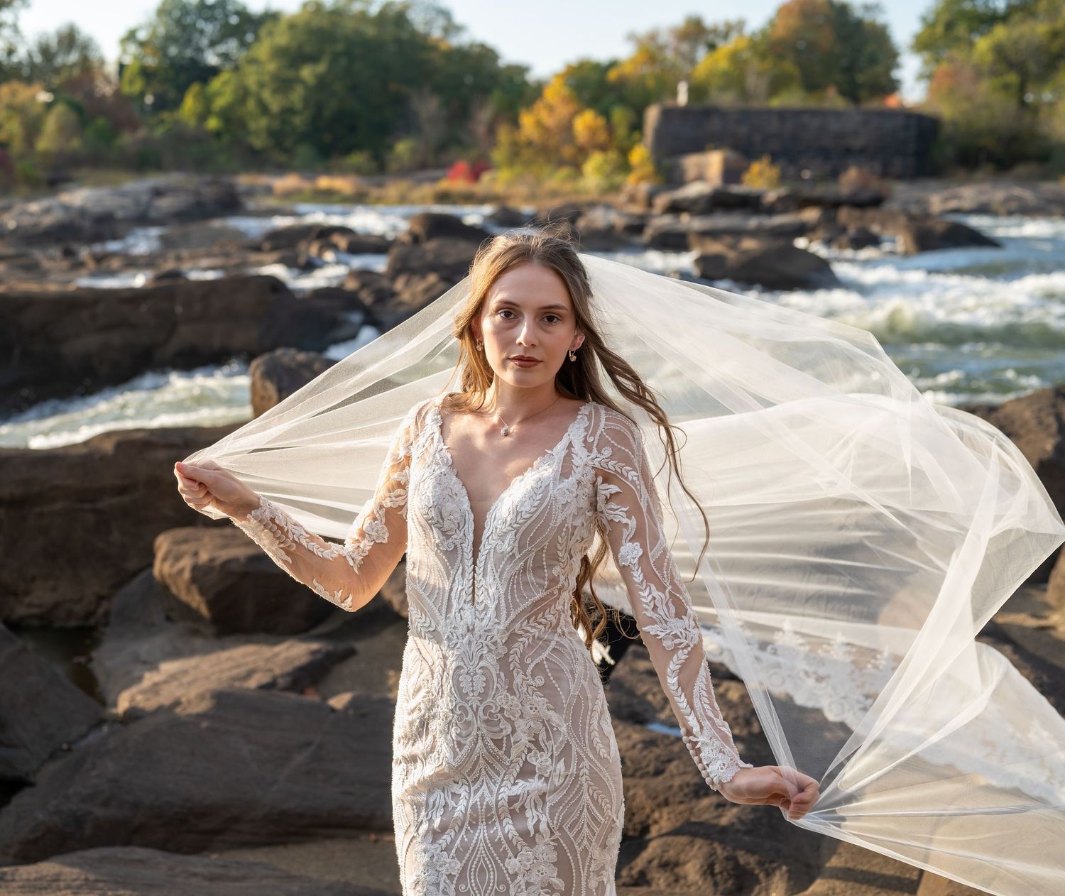 Long bridal veil billowing in the wind against a natural landscape with rocks and water.