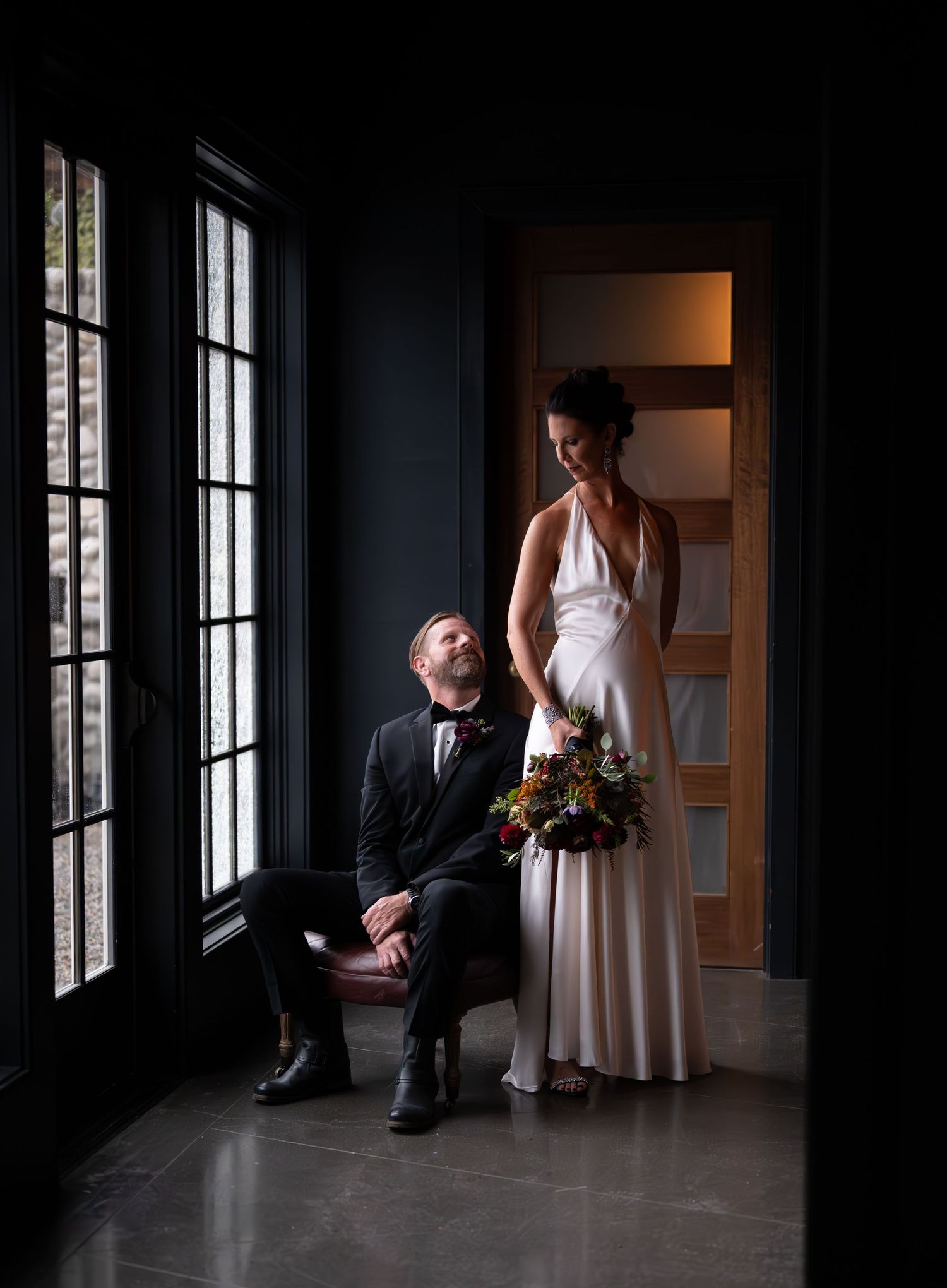 Dramatic indoor wedding photos with moody lighting and large windows creating silhouettes.