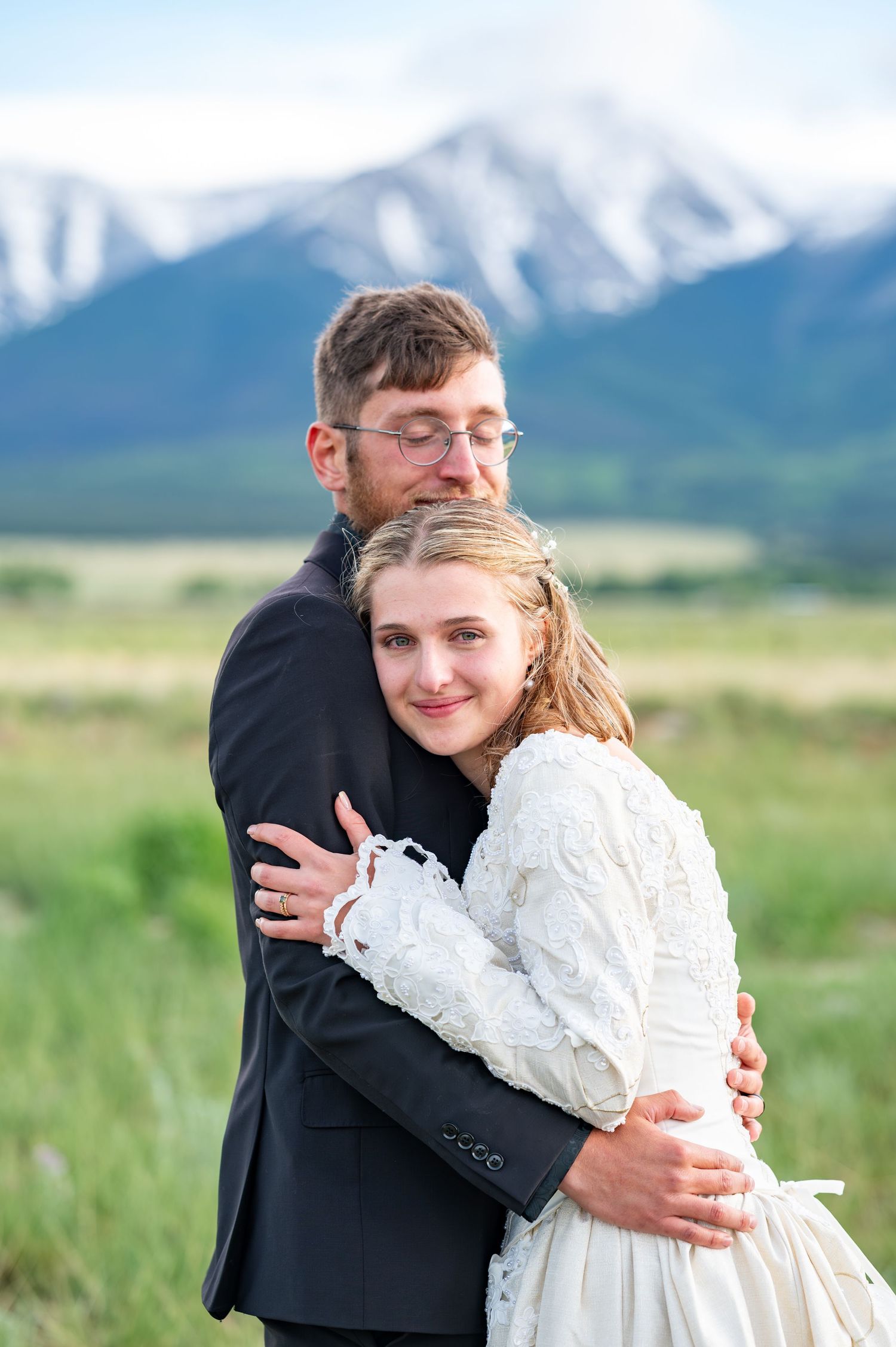 A tender embrace against a backdrop of snow-capped mountains and green meadows.