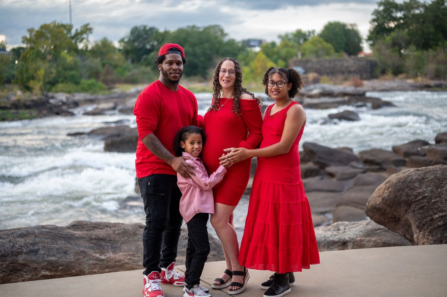 Family dressed in red outfits poses together on a beach with driftwood and waves in the background.