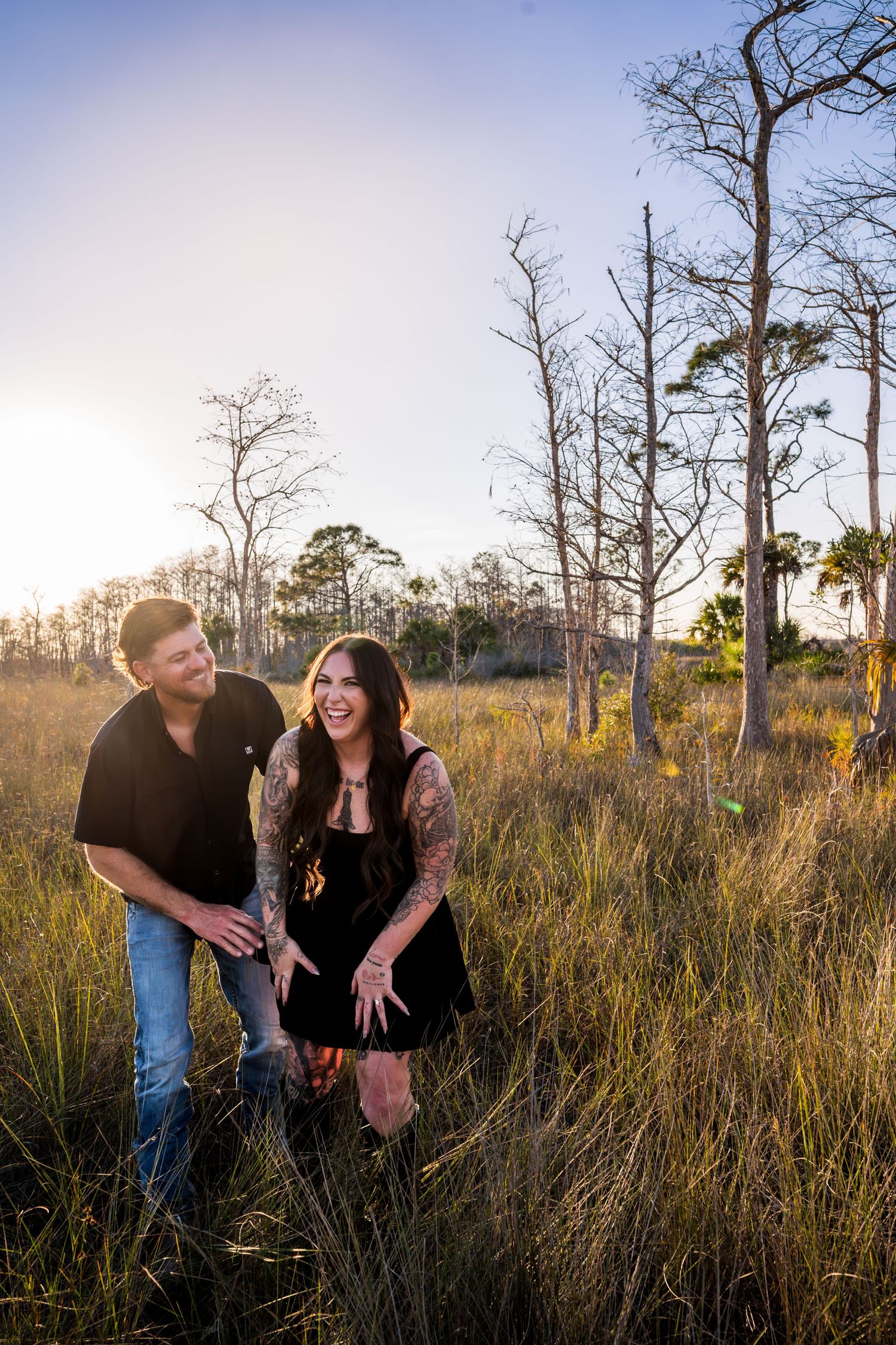 A romantic photoshoot in a field with tall grass and bare trees during golden hour.