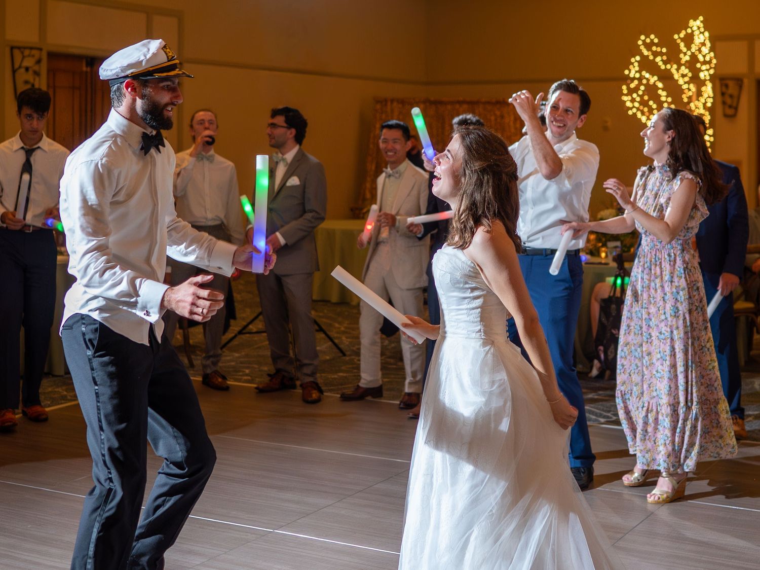 Guests dance and celebrate at a wedding reception with glowing decorations in the background.