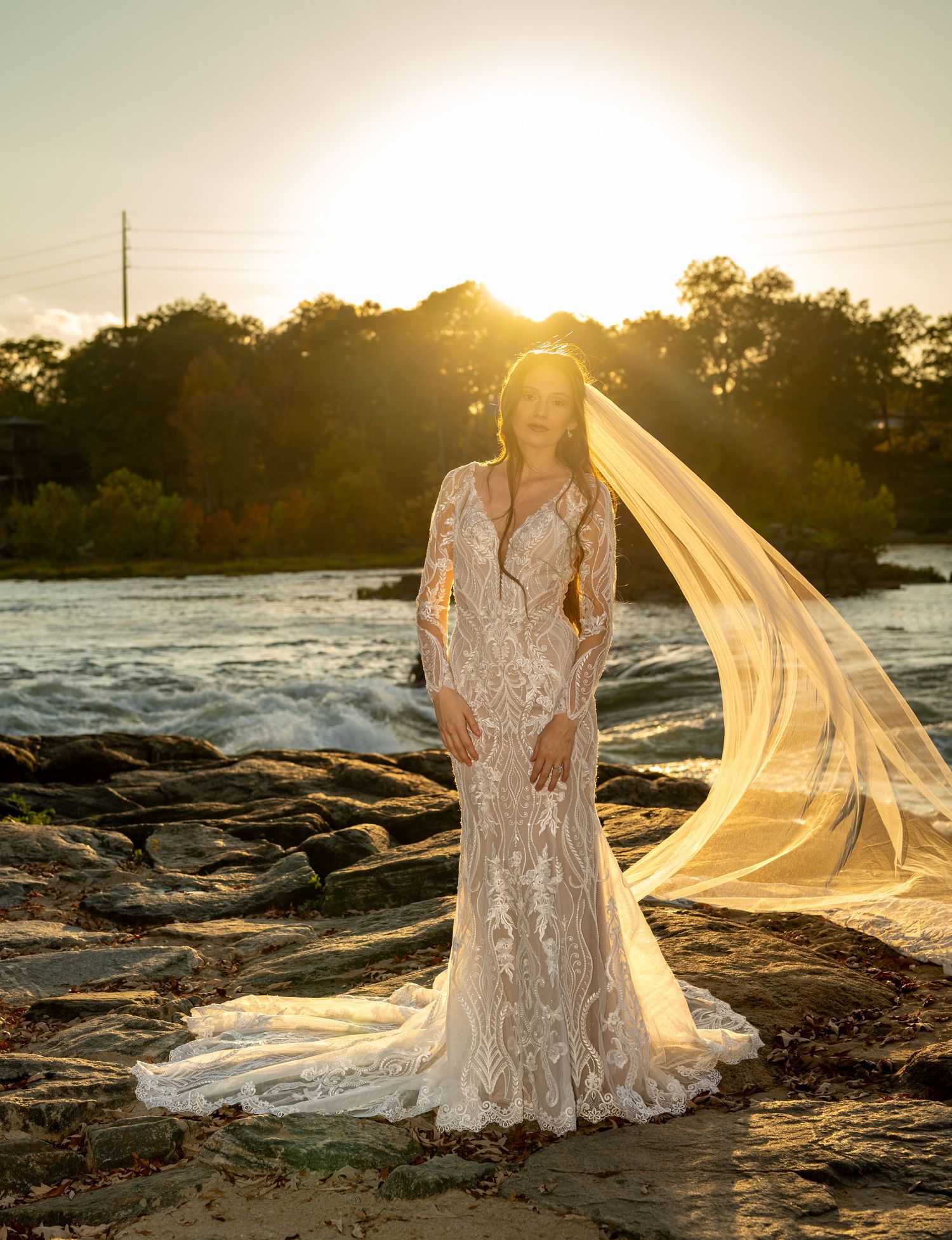 A dramatic sunset bridal photo on rocky terrain with flowing veil catching golden light.
